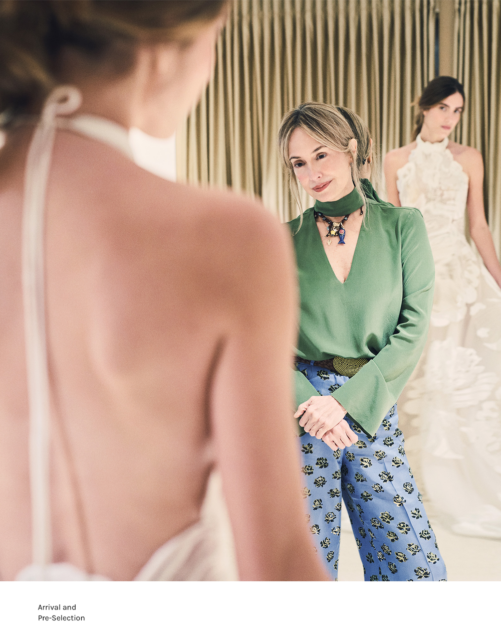 Woman in a green top and blue patterned pants standing between two models wearing wedding dresses.