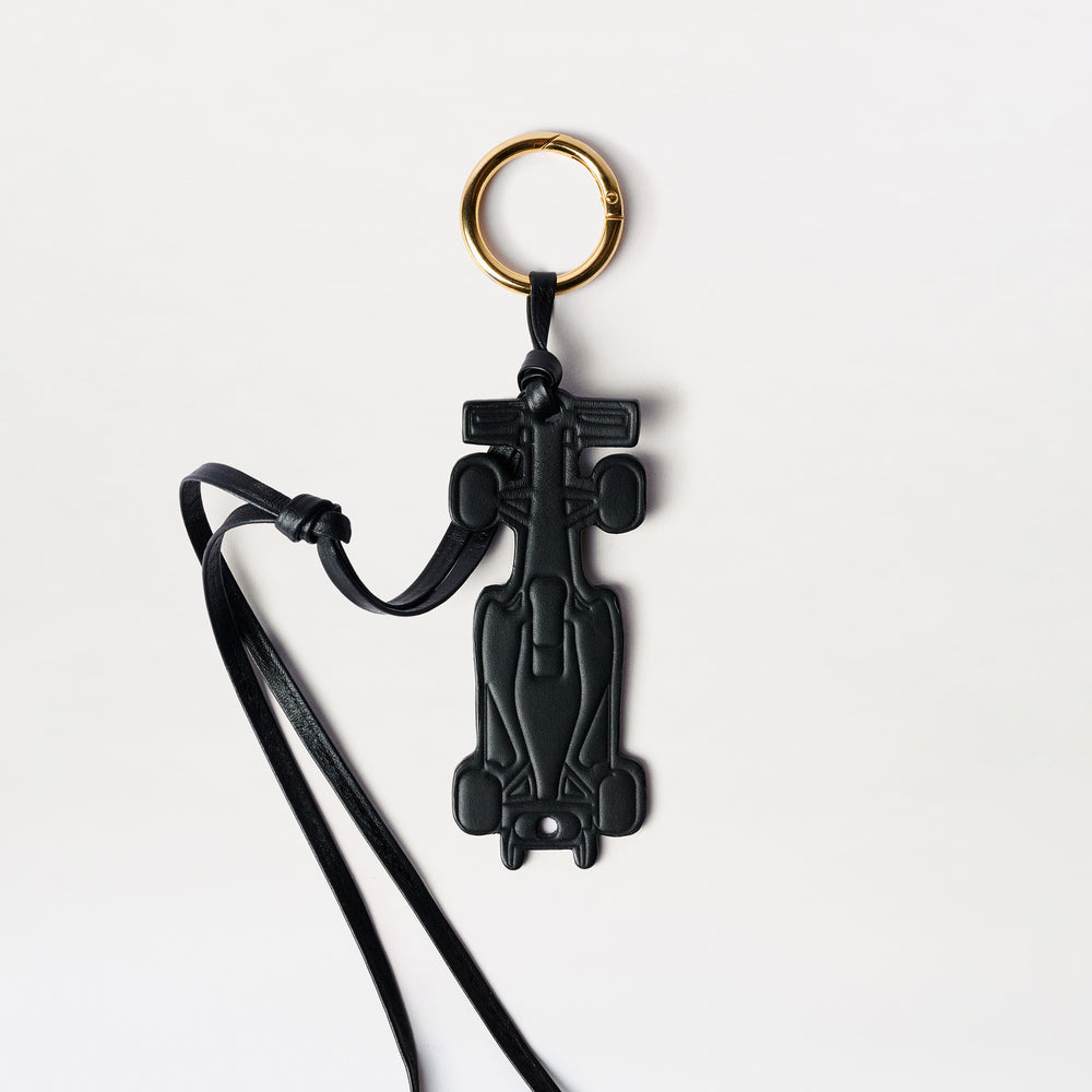 Race Charm: a black Formula 1 race car-shaped keychain featuring a gold-tone ring and an Italian leather strap, displayed on a white background.