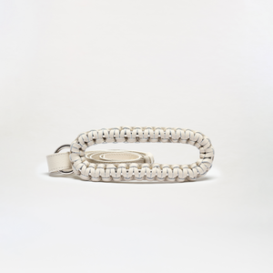 The Cloris Belt is a small, oval-shaped bag made in Colombia from braided white leather with black accents. It features an open center holding a matching coiled strap, and is shown on a plain white background.