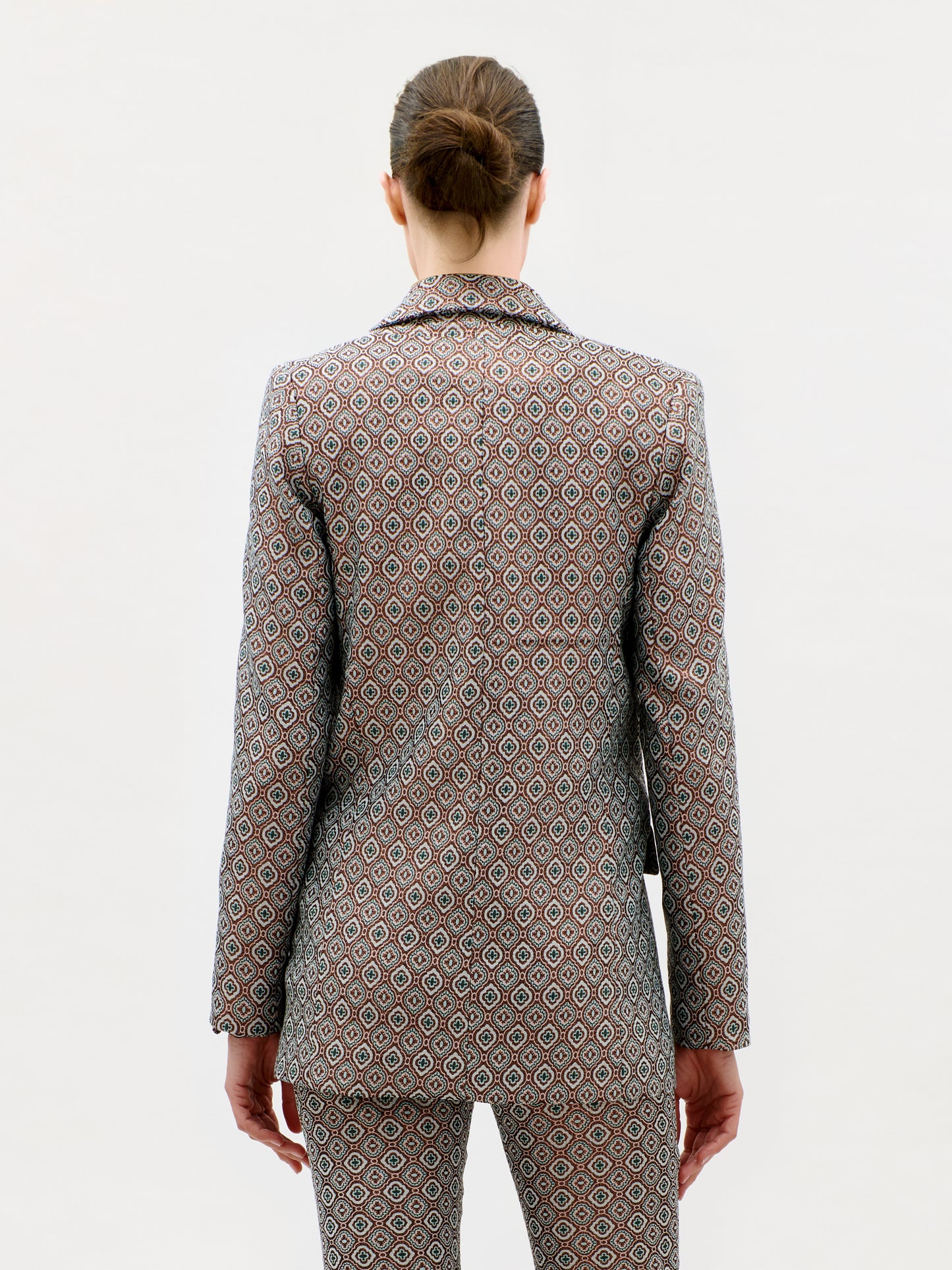 A person with brown hair in a bun is shown from the back against a plain white background, wearing the Cuneo Jacket and matching pants made in Colombia from patterned Italian fabric.