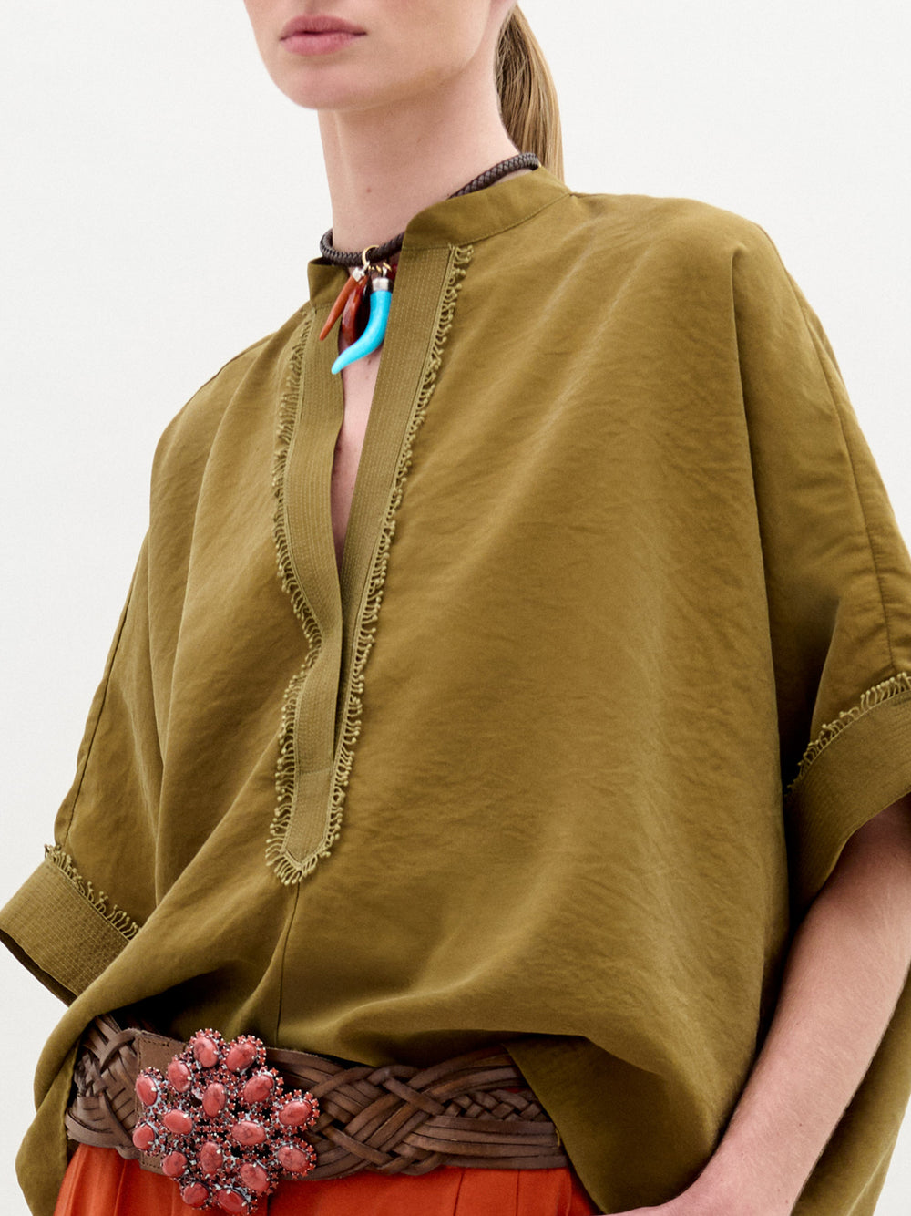 A person wearing the Daia Blouse in color Olive Opal with a brown belt on a white background.
