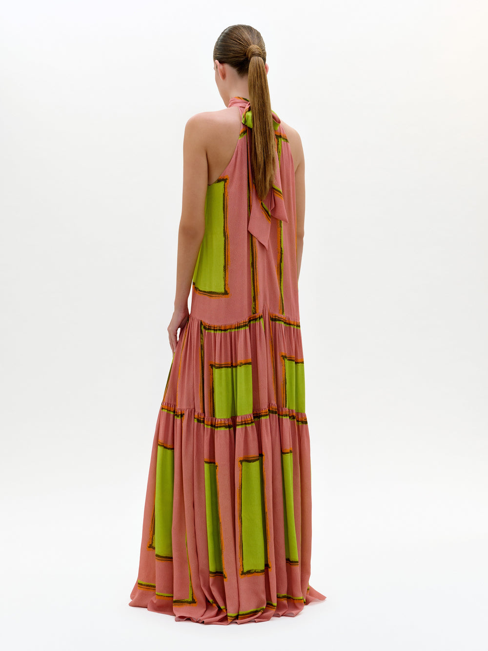 Woman wearing a long, halter-neck dress with green and pink pattern on a white background
