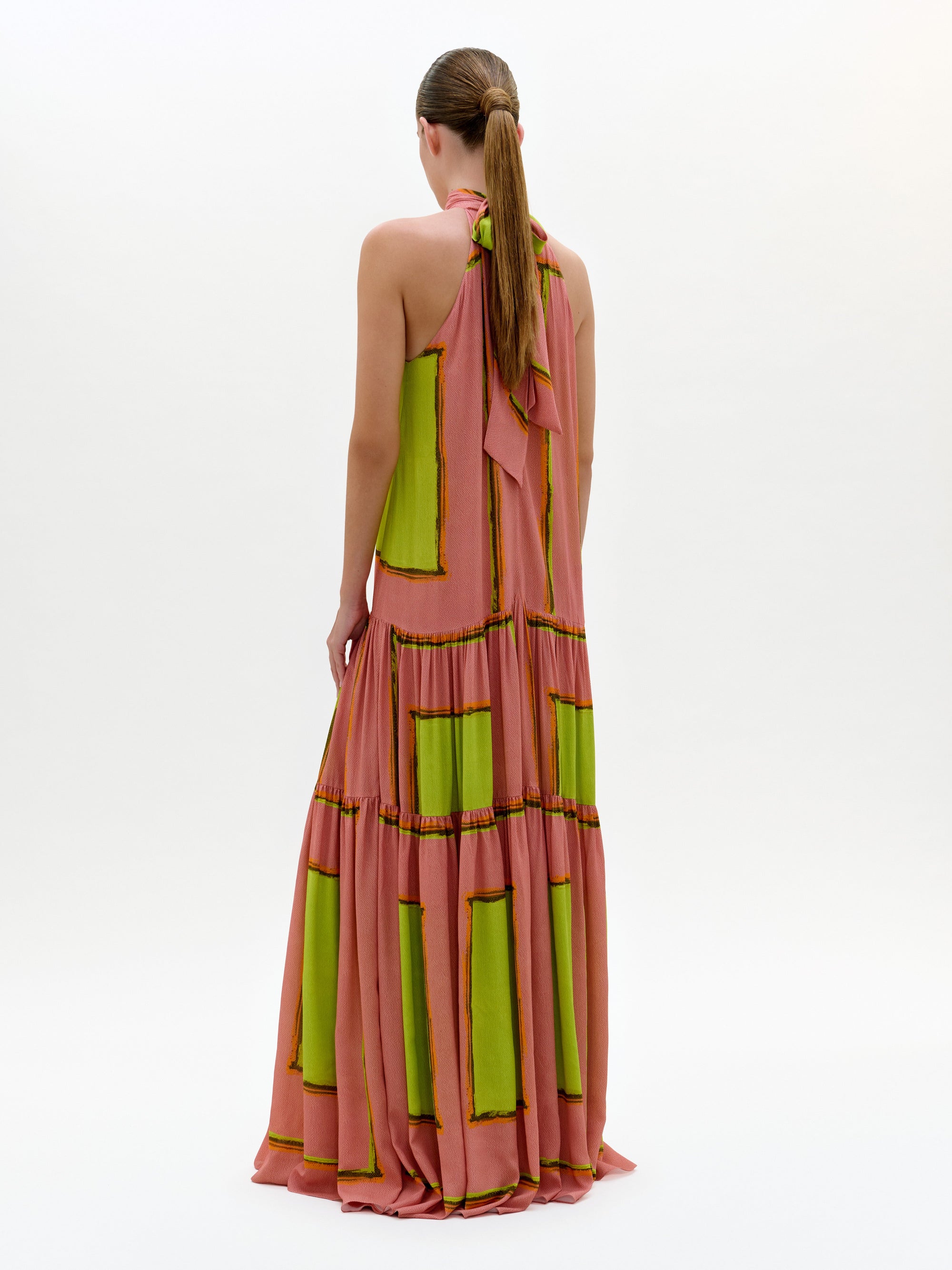 Woman wearing a long, halter-neck dress with green and pink pattern on a white background