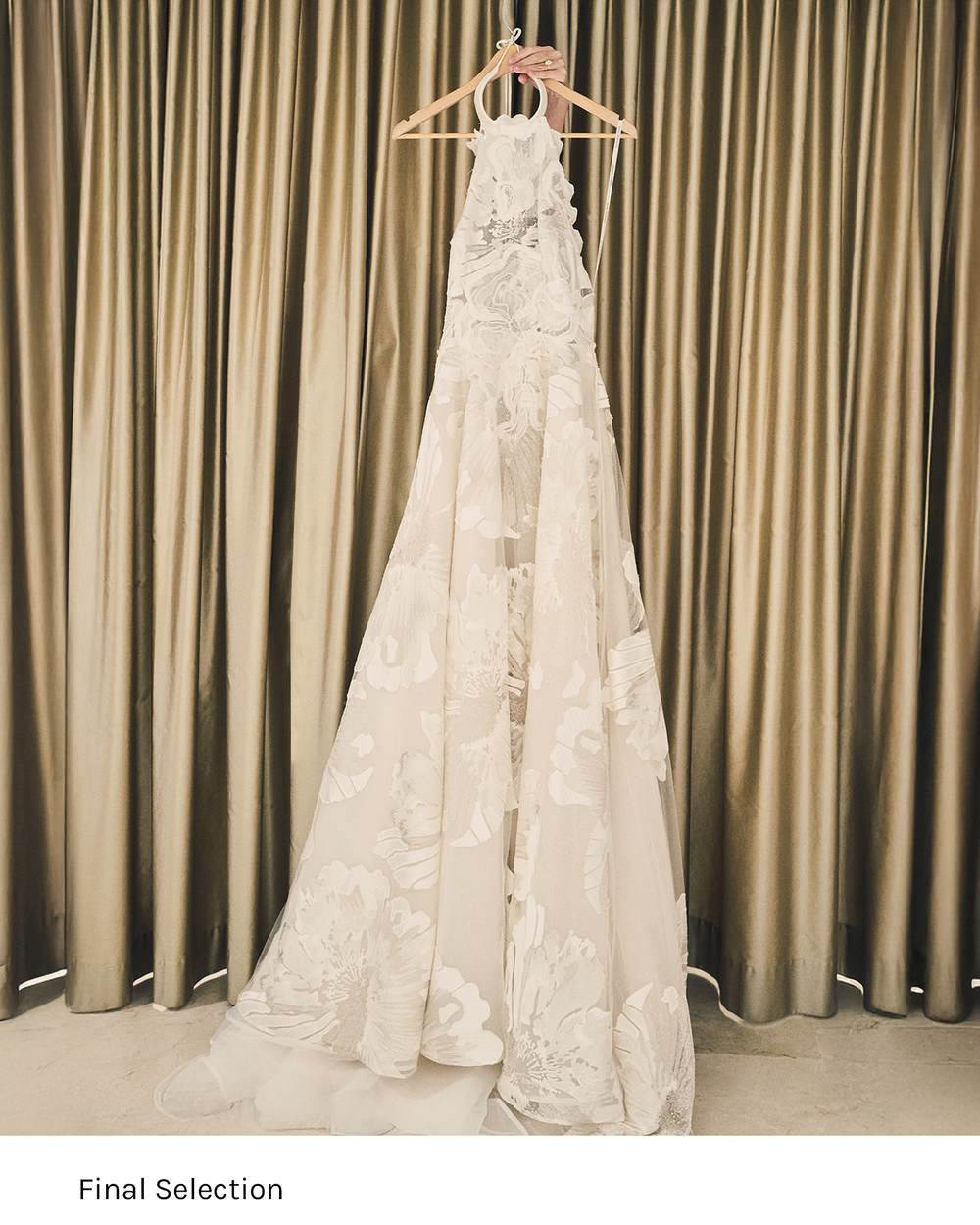 White lace wedding dress hanging against a beige curtain