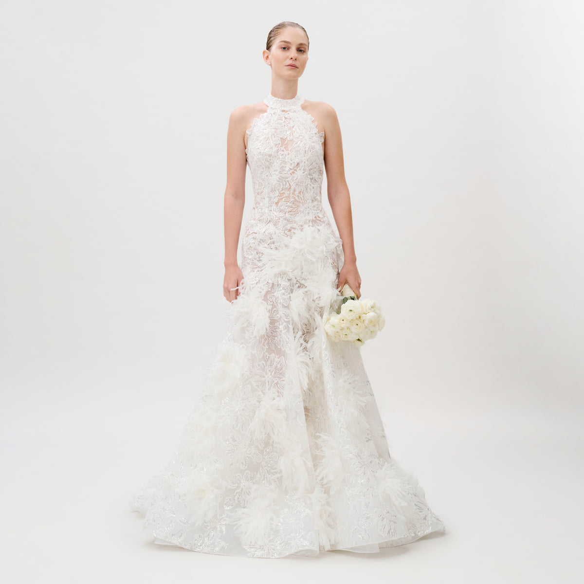 Dressed in the Darsha Dress, featuring delicate white lace and elegant silk trim, a person holds a bouquet of white flowers while standing against a plain white background.
