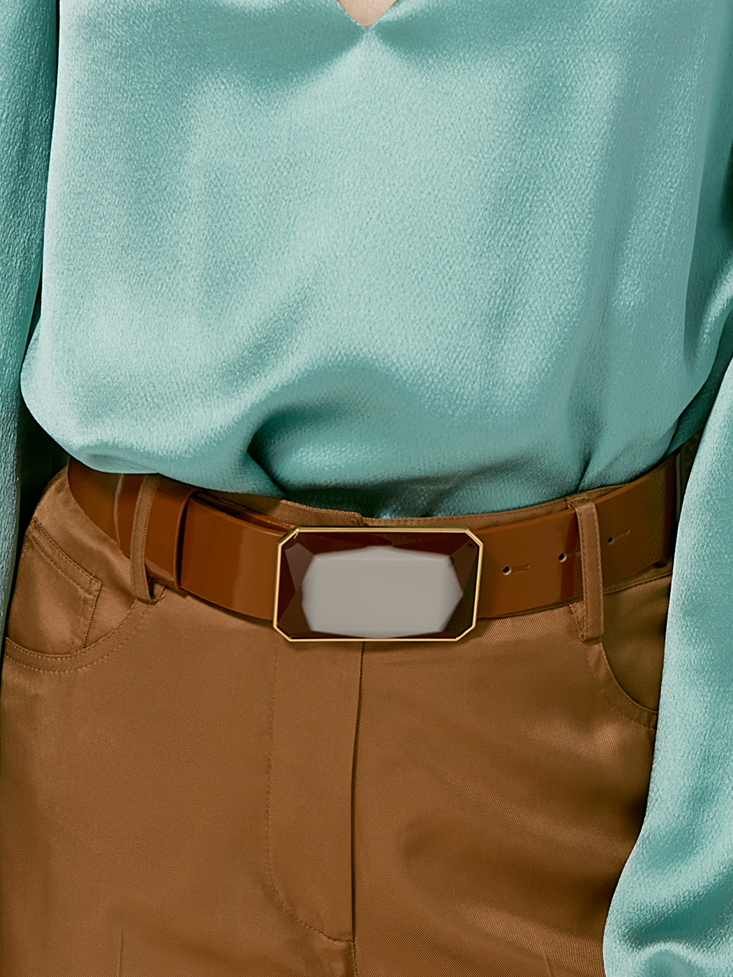 A person styled in a light teal blouse, high-waisted brown pants, and the Dora Belt—a wide brown belt with a large, rectangular gold-trimmed buckle.
