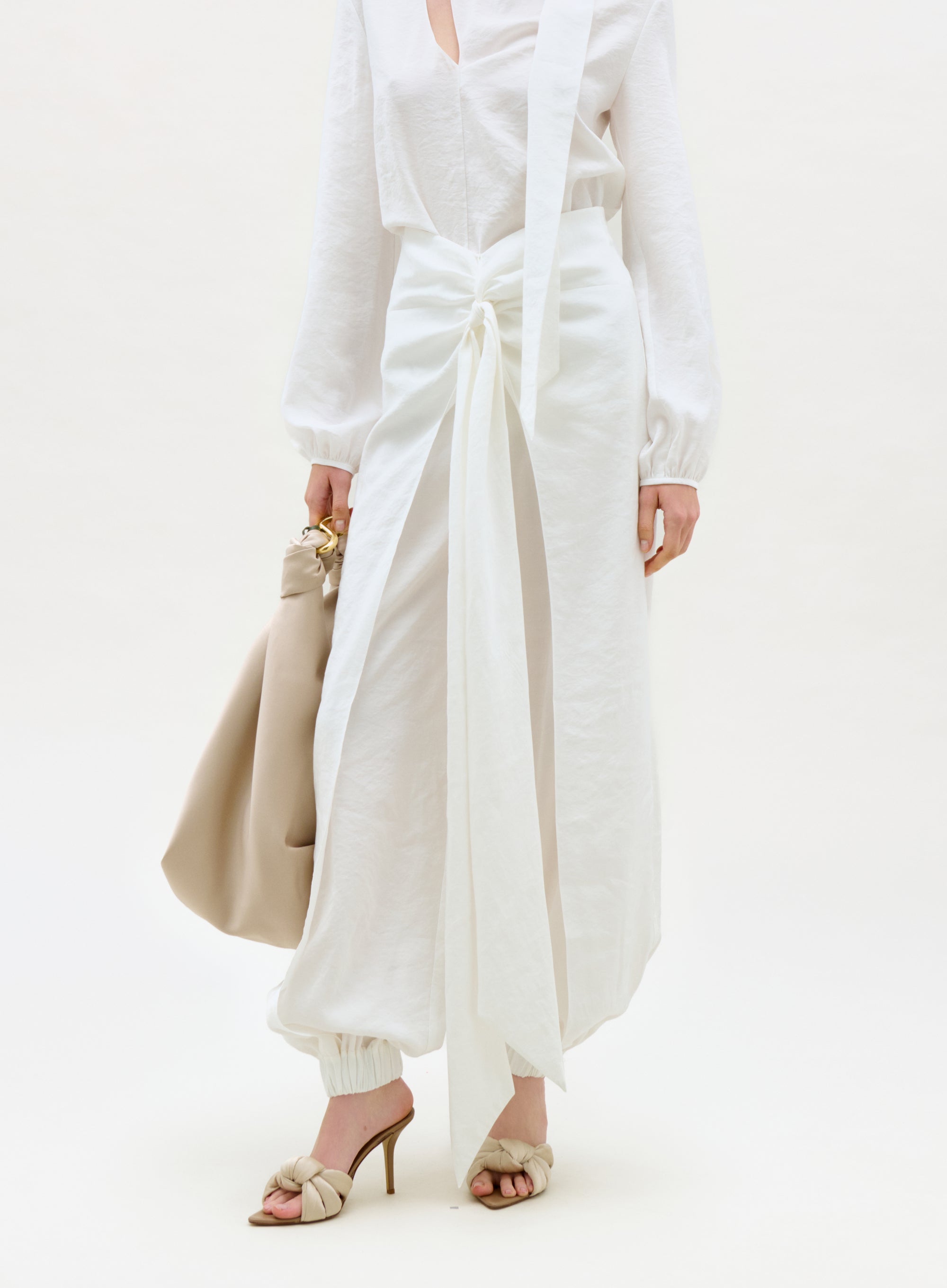 Person wearing a white outfit with wide-leg pants and holding a beige handbag on a white background