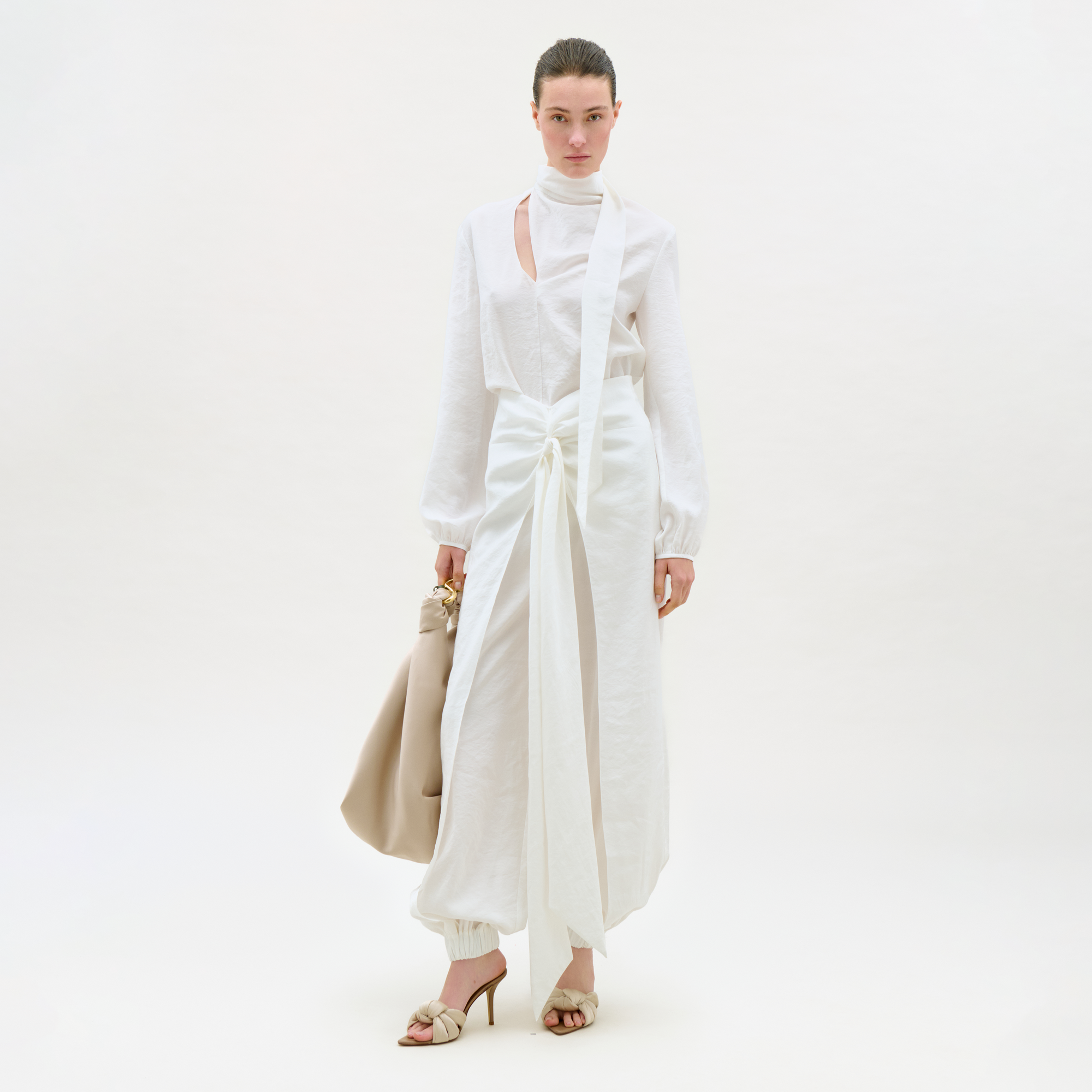 Woman wearing a white outfit with a beige handbag on a white background
