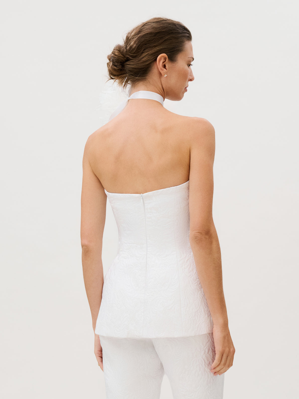 A woman with brown hair in an updo is seen from behind against a plain light background, wearing the strapless, textured Filomena Top and matching pants crafted from luxurious Italian fabric.