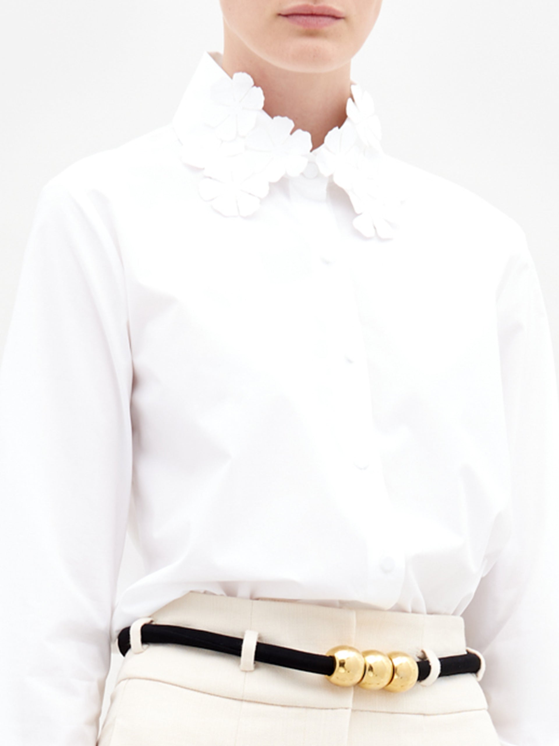 A person wearing the Flower Blouse  in color White with a golden belt on a white background.