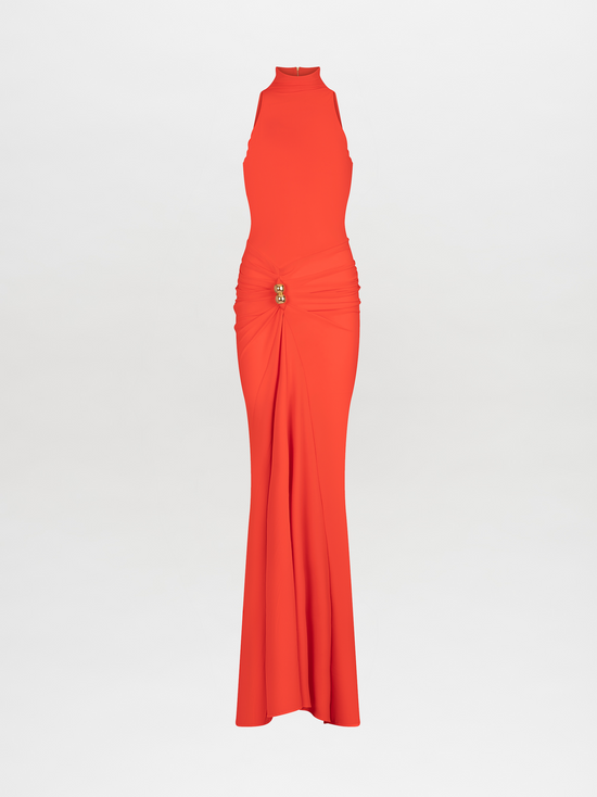 A woman in a long, sleeveless, high-neck orange Frances Dress Tangerine stands against a plain white background. The dress is gathered at the waist with a decorative clasp. This stylish piece is available for pre-order now and will ship by November 15th, 2024.