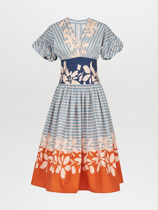 The Fulvia Dress Celeste Orange captivates with an off-the-shoulder silhouette, accentuated by blue stripes and a navy waistband. The dress features charming floral patterns in peach and orange on the top and bottom sections, striking a delightful balance between elegance and playful style.