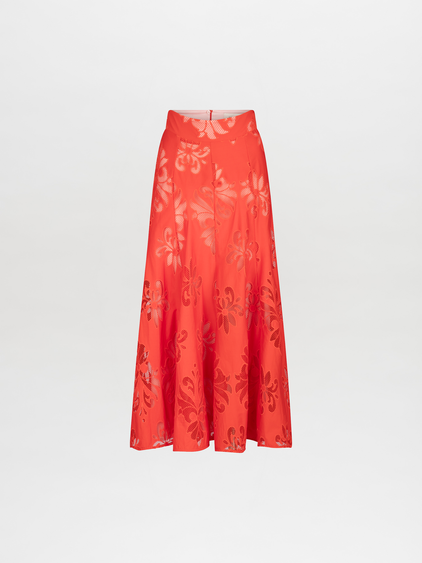 A woman stands wearing a Grettel Skirt Rouge Embroidery with a bright orange floral-patterned two-piece outfit and colorful sandals. She poses against a plain white background, available for pre-order starting November 15th for the 2024 collection.