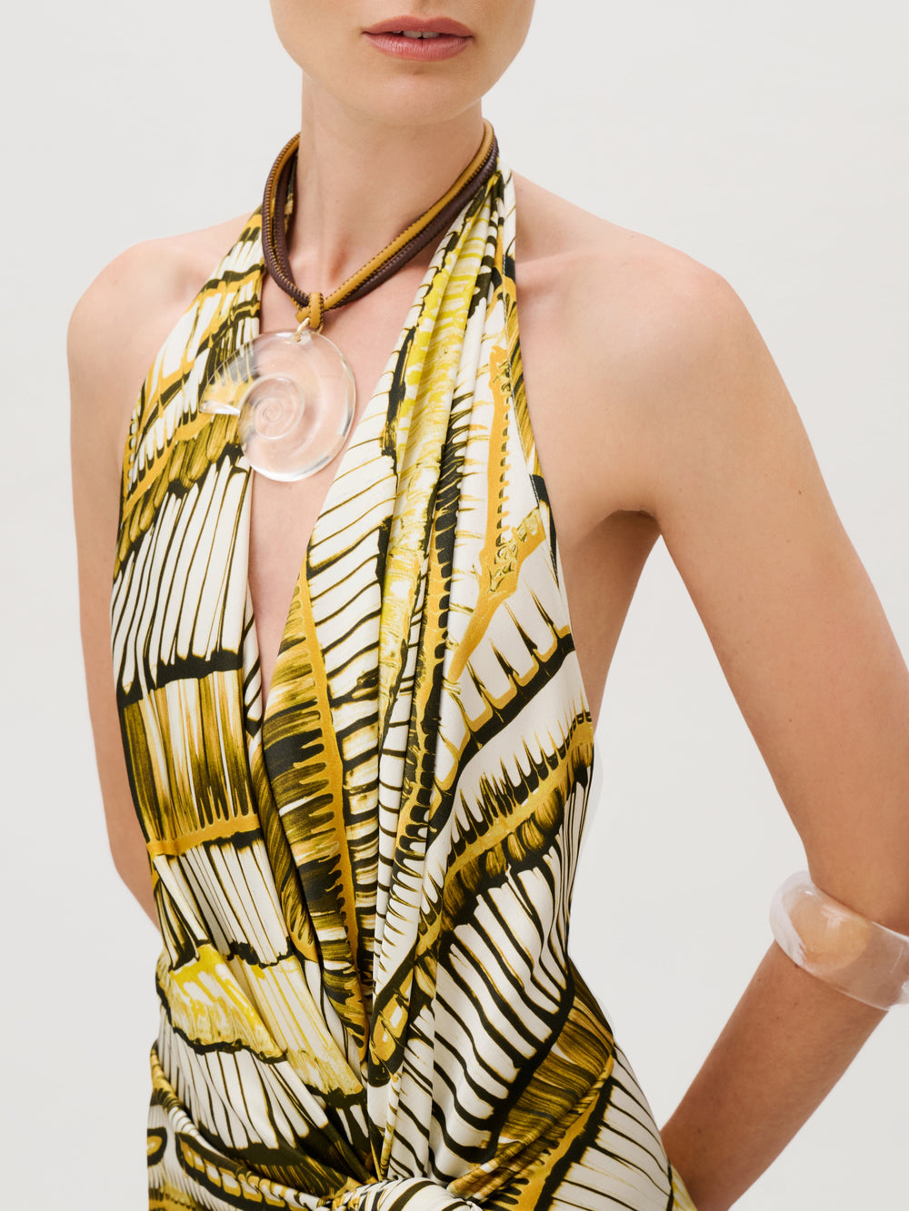 The Guadalupe Dress in an Italian crepe satin with a yellow and black abstract pattern, worn with a large clear shell pendant on a brown cord and a matching translucent bangle.