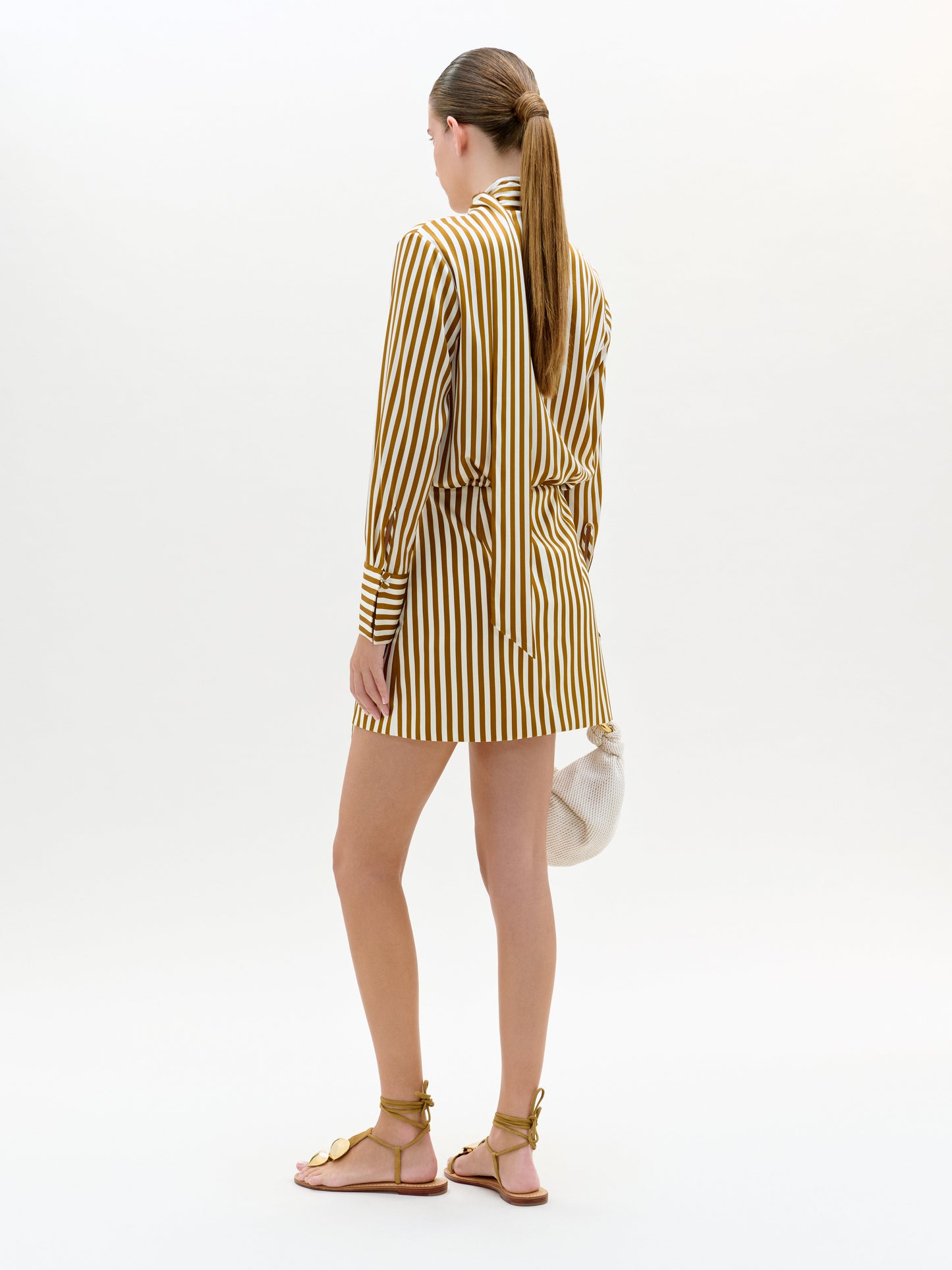 Woman wearing a yellow and white striped blazer over a dress on a white background