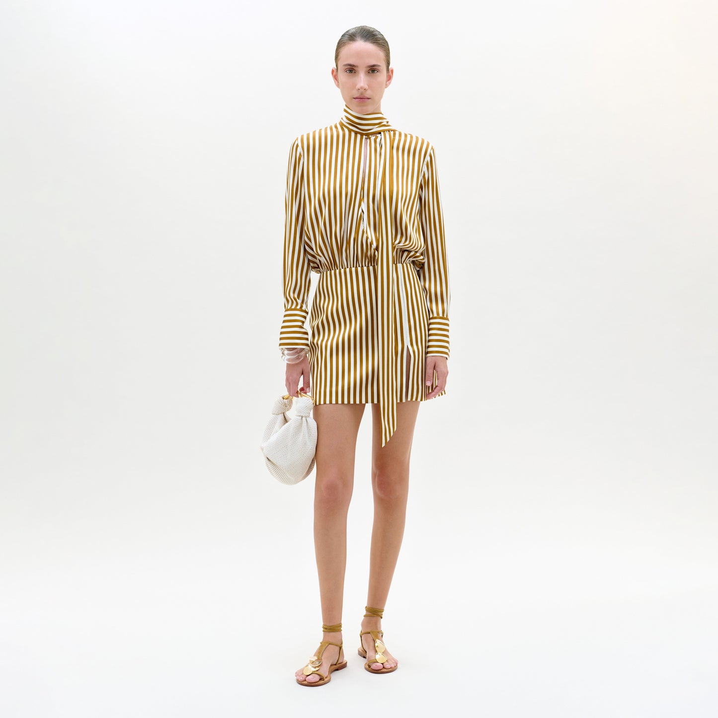Woman wearing a gold and white striped dress on a white background