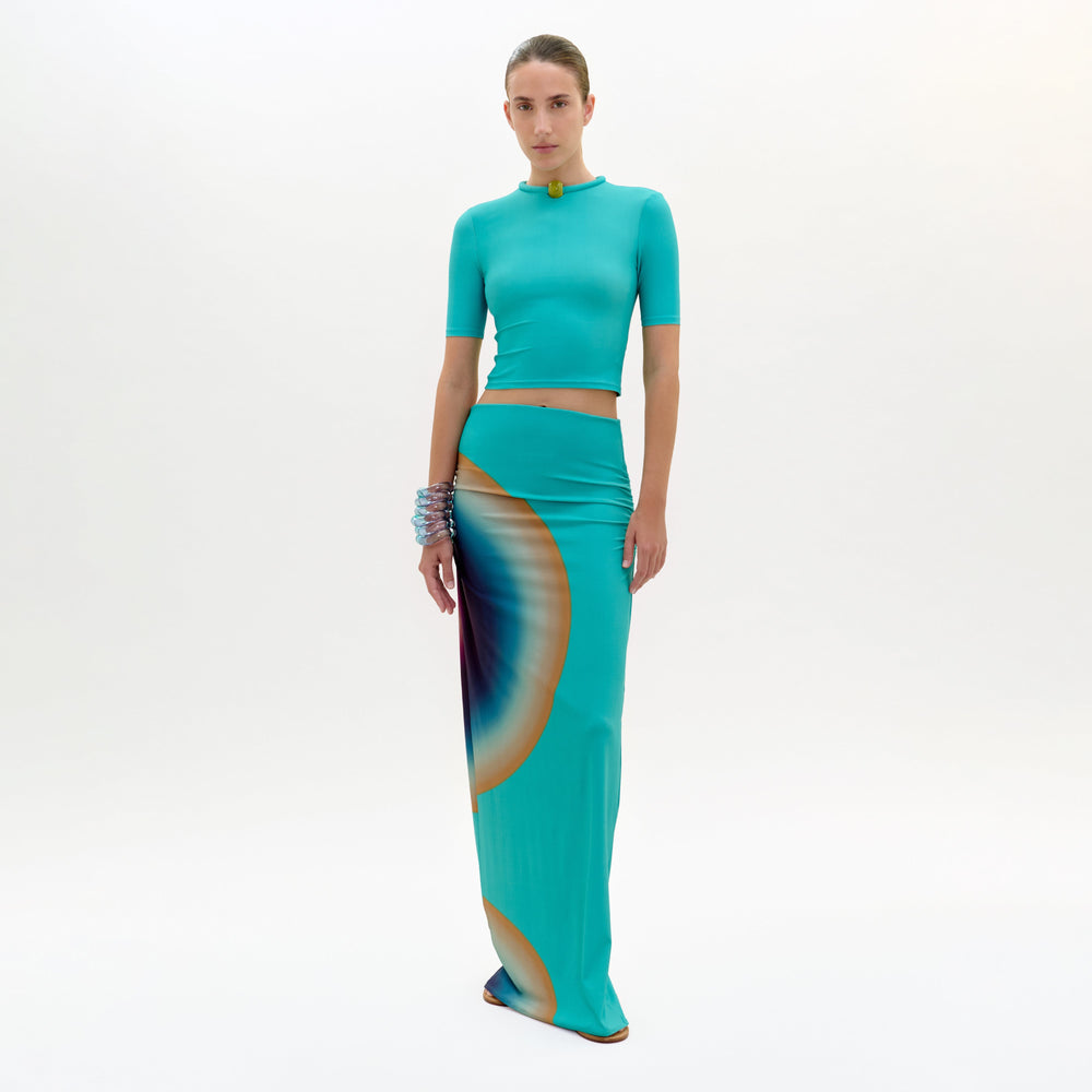 Woman wearing a teal outfit with a colorful skirt on a white background