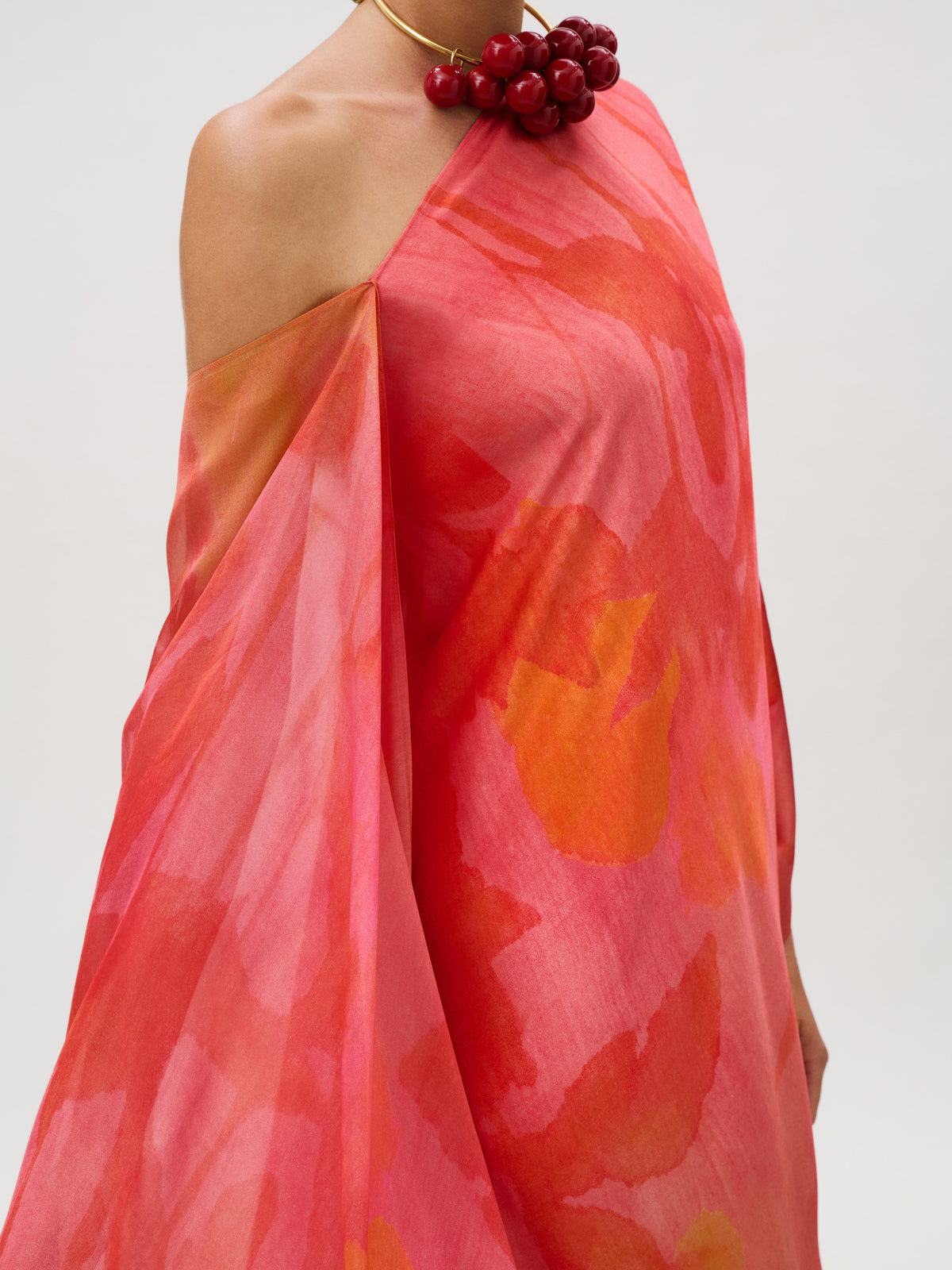 Jade Dress in a one-shoulder silk chiffon floral print featuring pink and orange tones, styled with a red beaded statement necklace.