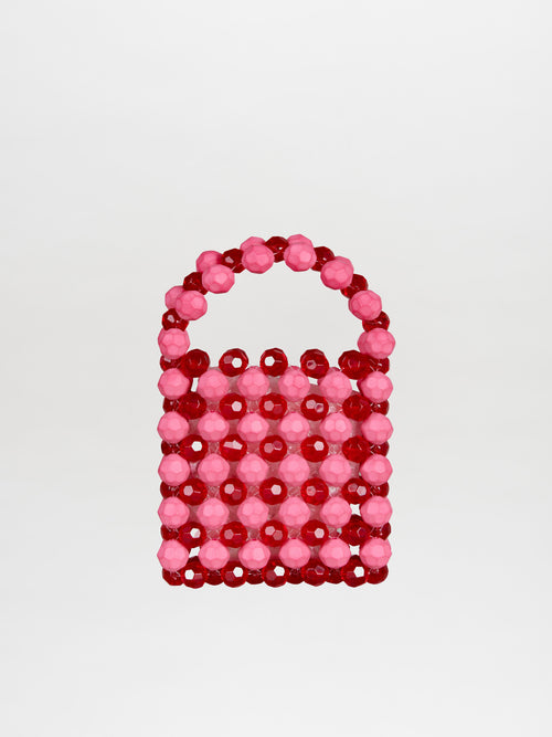 The Jasy Handbag Vermillon-Pink is a small, rectangular handbag adorned with red and pink beads, featuring a round bead handle that creates a textured effect against its plain background.