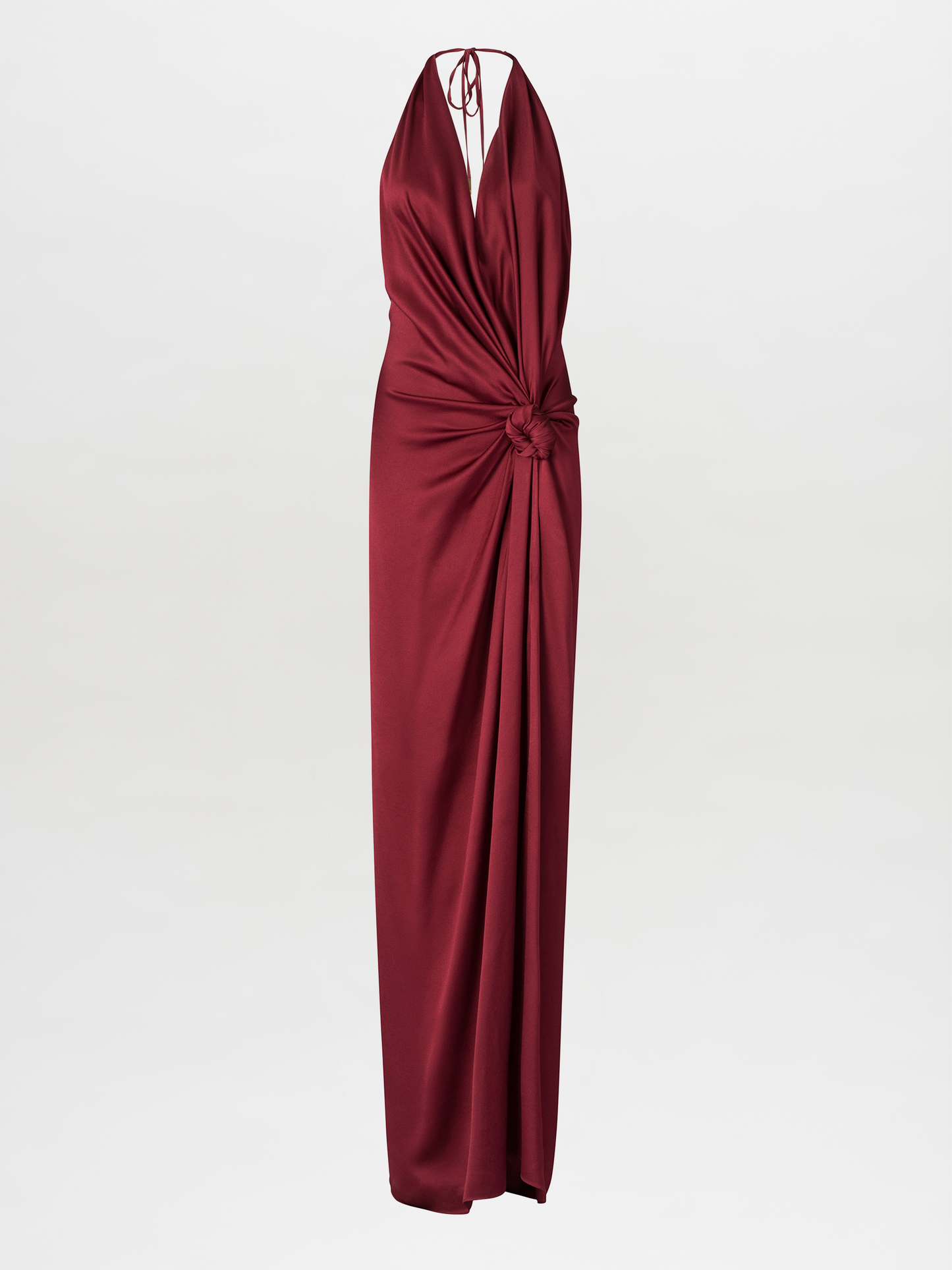 The Jazmin Dress in Burgundy is a long satin halter-neck maxi dress featuring a deep red hue and a knot detail at the waist, showcasing a draped silhouette that elegantly flows down to the hem.