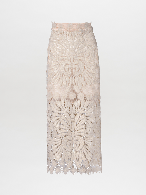 The Kin Skirt Gold, a high-waisted beige lace pencil skirt featuring intricate floral patterns and a sheer hem embellished with subtle metallic detailing, elegantly stands out against a plain white background.