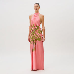 The Koori Dress is a floor-length pink silk halter dress featuring a green floral-like print gathered at the center waist.