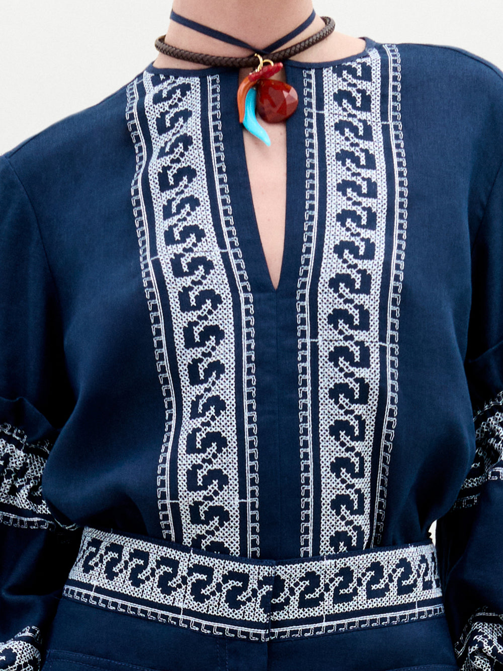 A woman stands against a plain white background wearing the Lucaya Blouse—an embroidered navy blue linen top with voluminous sleeves—paired with matching navy trousers.