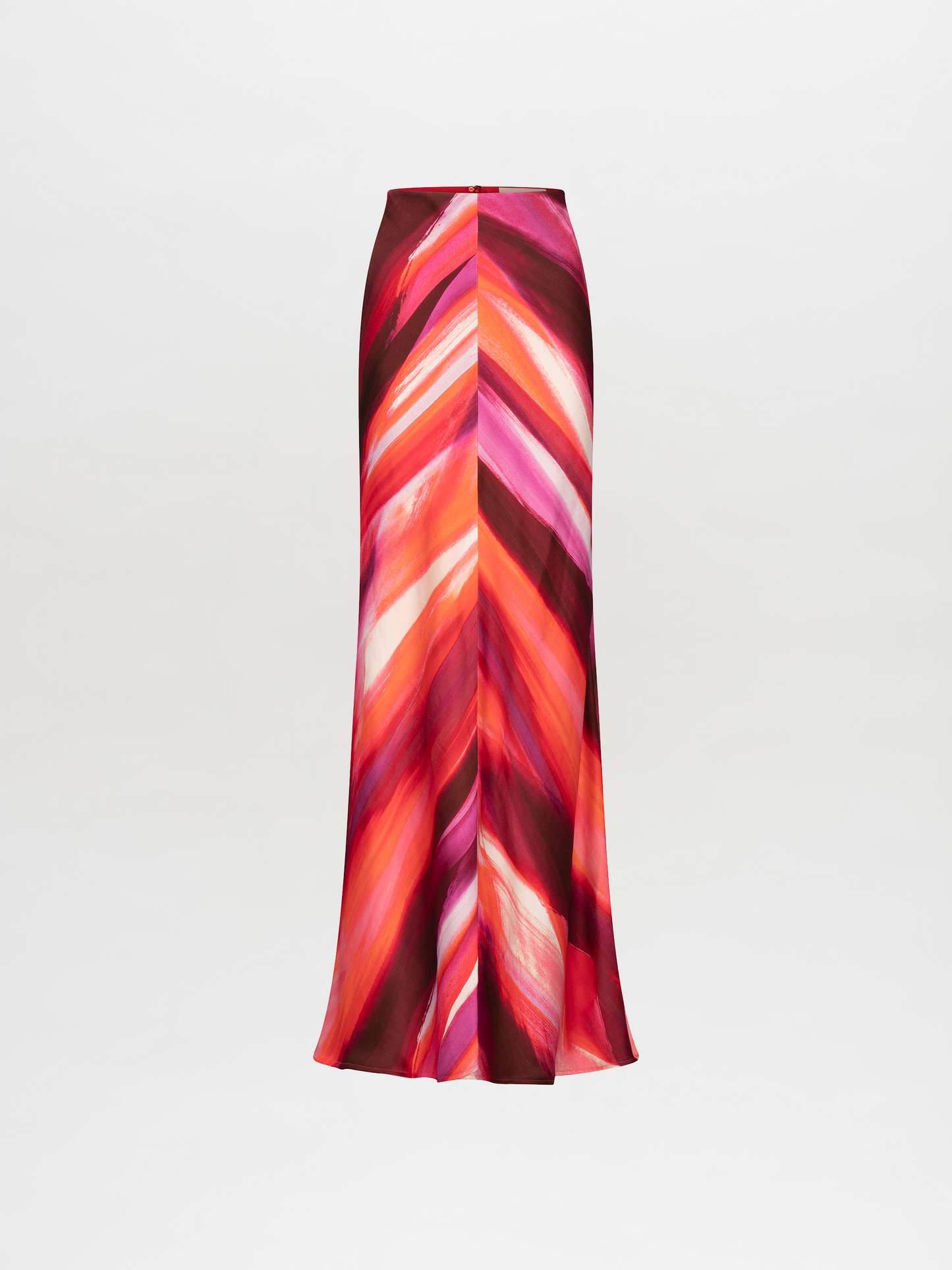 A person stands against a plain background, wearing a vibrant suit in red, pink, and orange streaks, paired with the Laurina Skirt Magenta Abstract Waves and bold gold necklace. This stunning ensemble will be available for pre-order soon and is set to ship by date 2024.