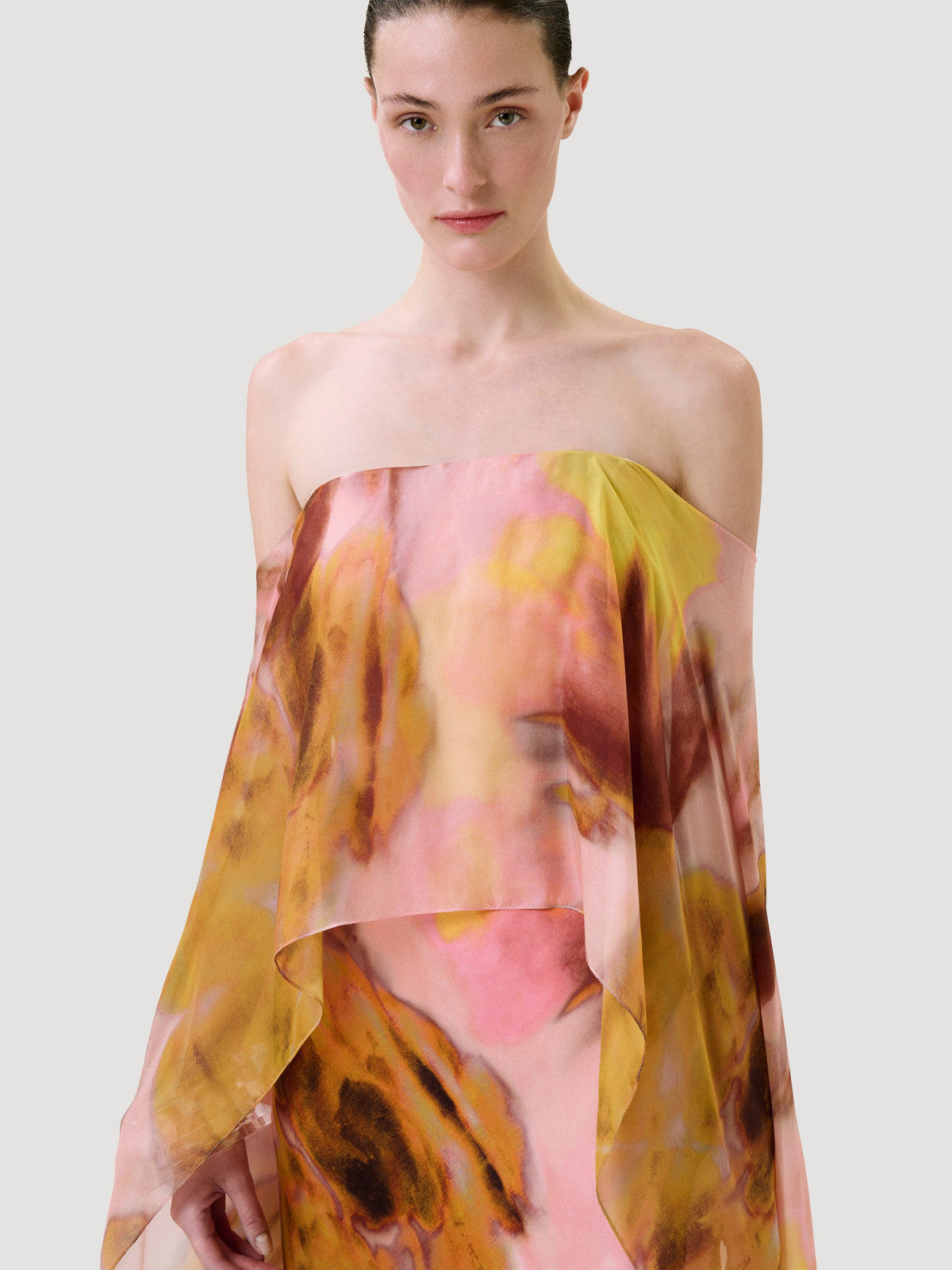 A model wears the Lovane Dress, a strapless, tiered design featuring an abstract pink and yellow watercolor print.