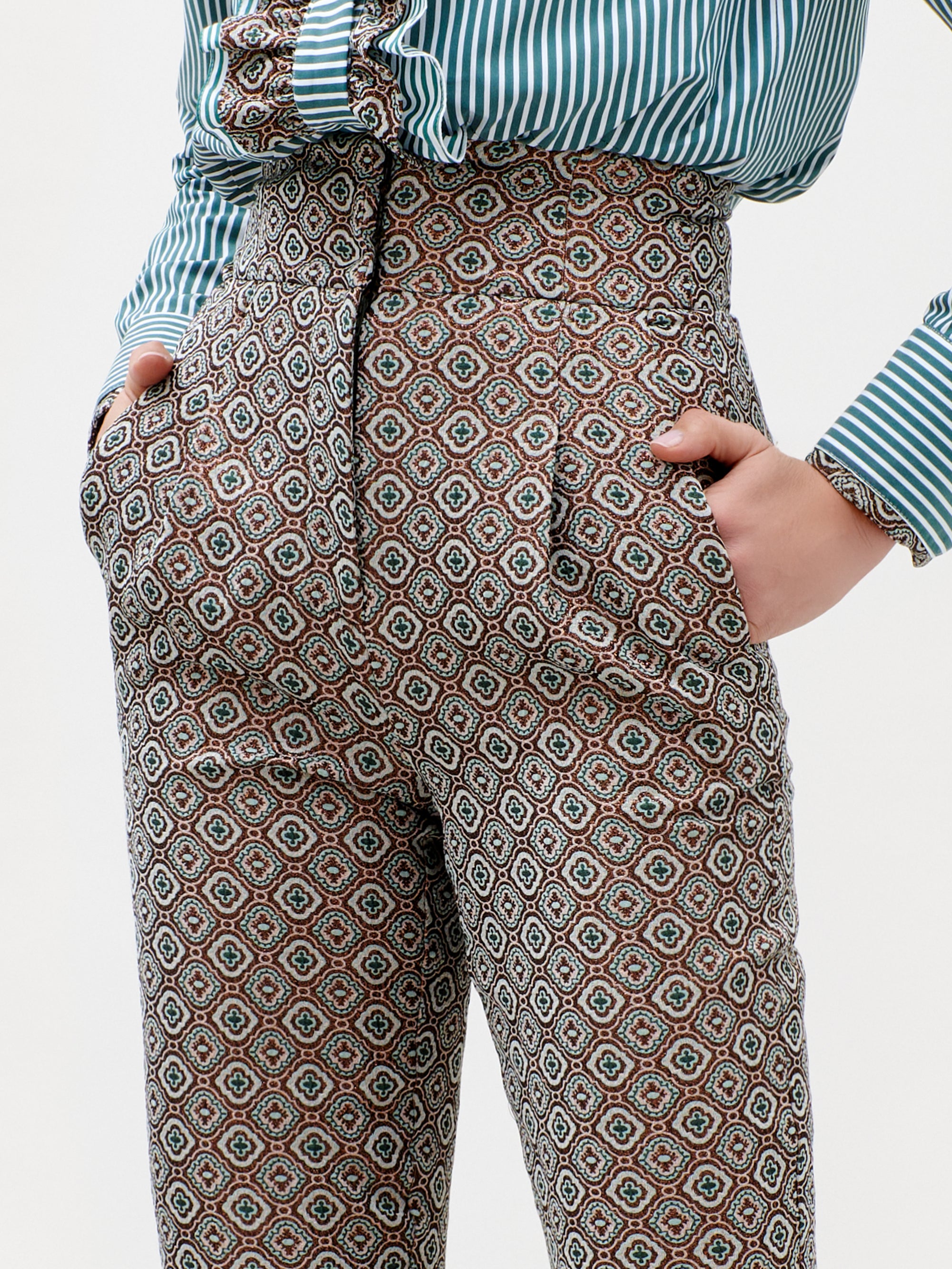 Person wearing the Luca Pant—high-waisted and patterned, crafted from luxurious Italian fabric—with hands in pockets and a green-and-white striped shirt. The image centers on the pants and part of the shirt; head and lower legs are not visible. Made in Colombia.