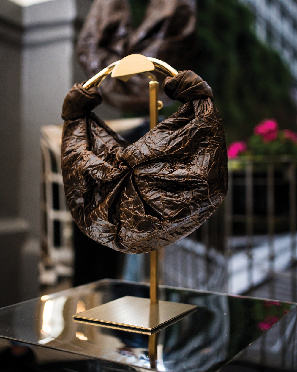Brown textured handbag on a gold stand with a blurred indoor background