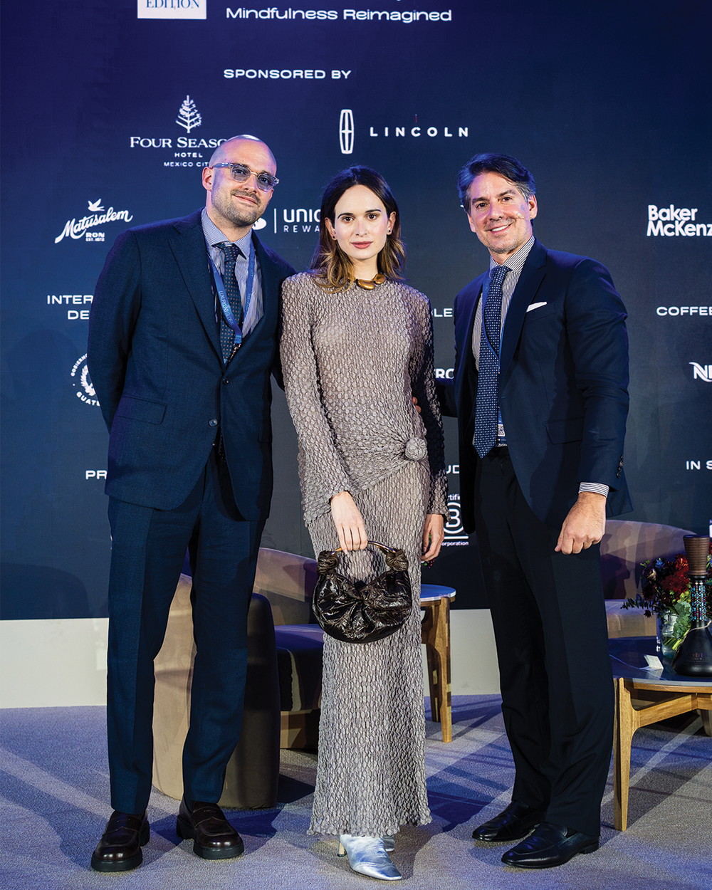Three people posing together at an event with sponsor logos in the background