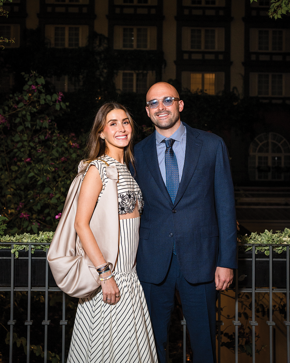 Man and woman posing outdoors at night in formal attire with a building in the background.