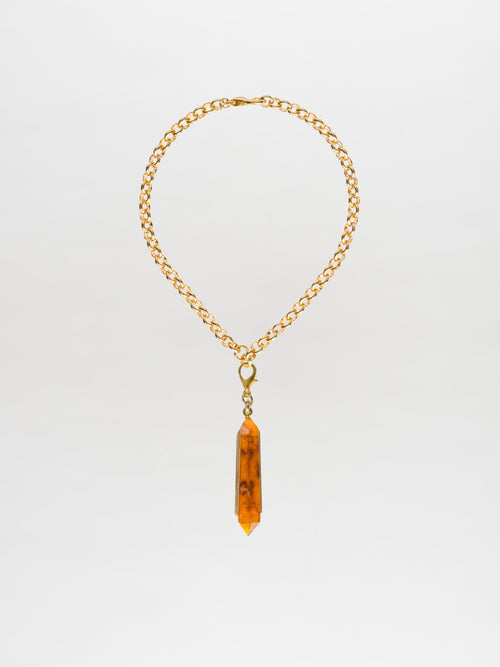 The Mariela Necklace Amber features a chic choker style, with a gold-plated brass chain adorned by a geometric crystal pendant in an amber hue.