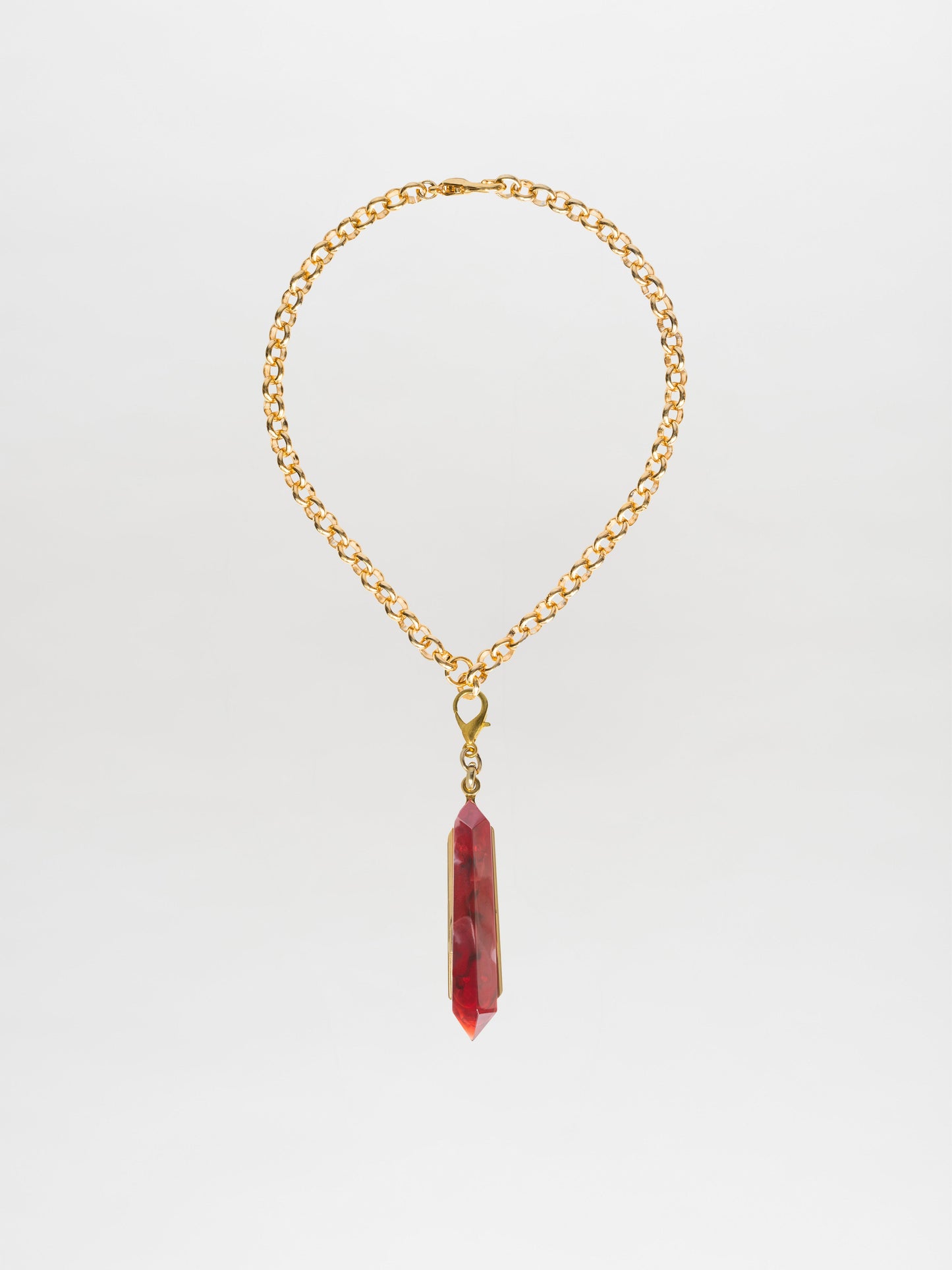 Introducing the Mariela Necklace Rouge: a gold chain choker featuring a striking geometric crystal pendant in red, showcased against a clean white background.