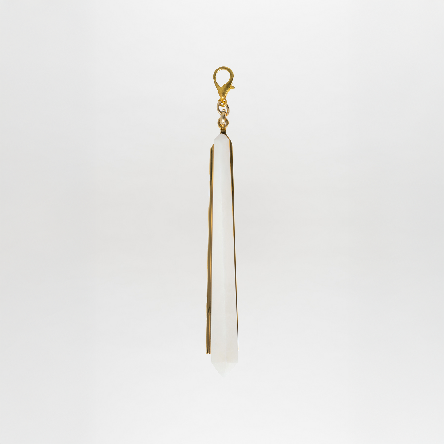 The Montse Charm features a long, pointed crystal pendant with a gold-plated brass clasp, set against a plain white background.