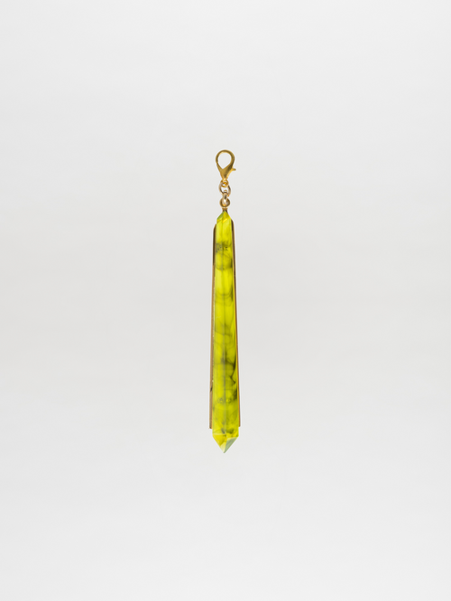 A long green crystal charm pendant featuring black marbling, with a gold-plated brass loop at the top, set against a plain white background.