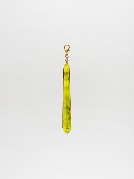 A long green crystal charm pendant featuring black marbling, with a gold-plated brass loop at the top, set against a plain white background.