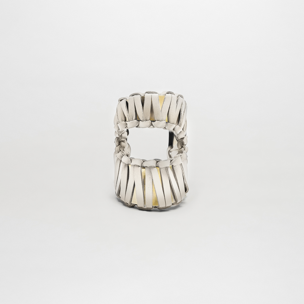 The Majel Cuff is a white sandal featuring thick, woven leather straps and a subtle gold-plated buckle, shown from the front against a plain white background.