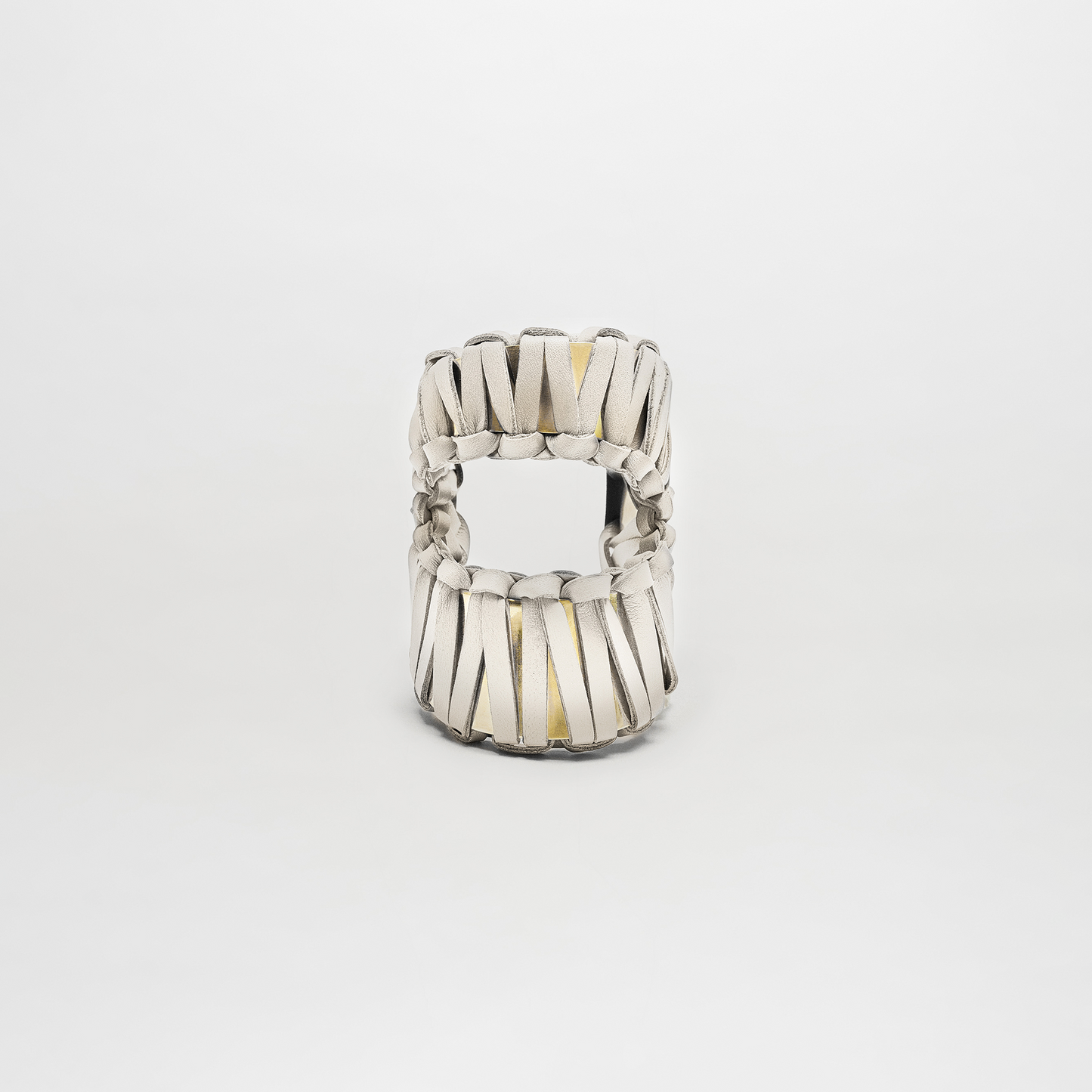 The Majel Cuff is a white sandal featuring thick, woven leather straps and a subtle gold-plated buckle, shown from the front against a plain white background.