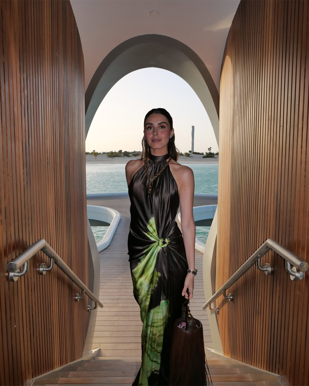 Woman in a black and green dress standing on a wooden deck with a waterfront background