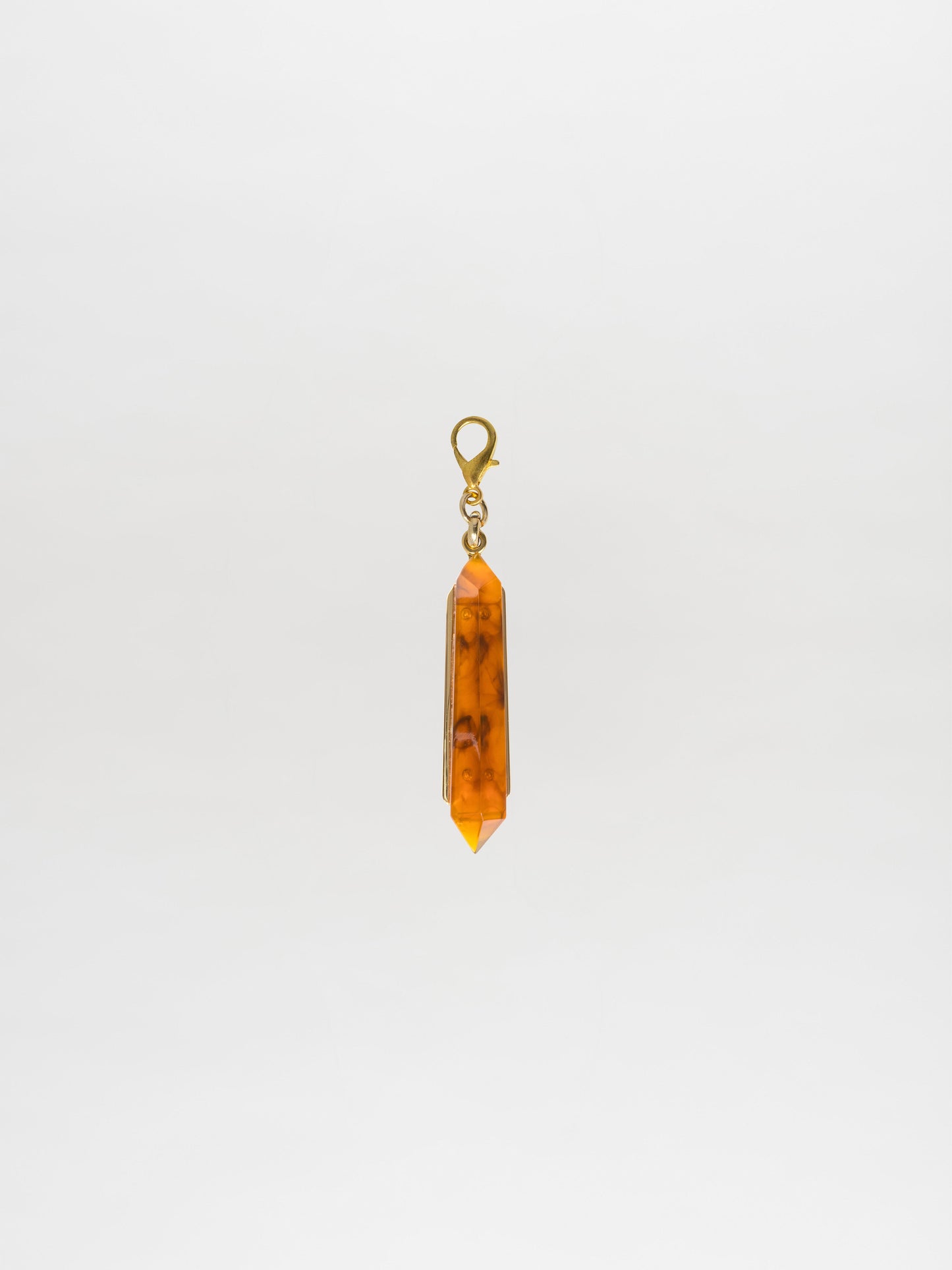 Presenting the Mariela Charm Amber: a pendant featuring an orange crystal with a metal clasp, showcasing a Petralux® fantasy stone against a plain white background.