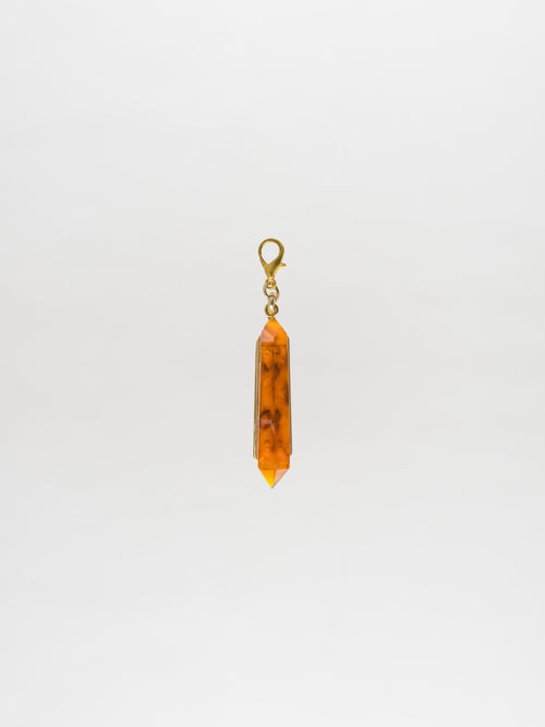 Presenting the Mariela Charm Amber: a pendant featuring an orange crystal with a metal clasp, showcasing a Petralux® fantasy stone against a plain white background.