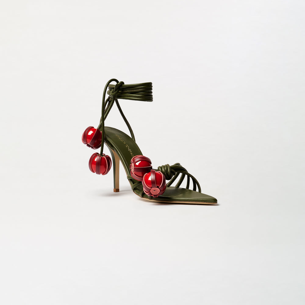 The Mele Heels are high-heeled sandals, expertly crafted from Italian leather, featuring olive green straps adorned with large red bead embellishments and an elegant ankle wrap tie, displayed on a plain white background.