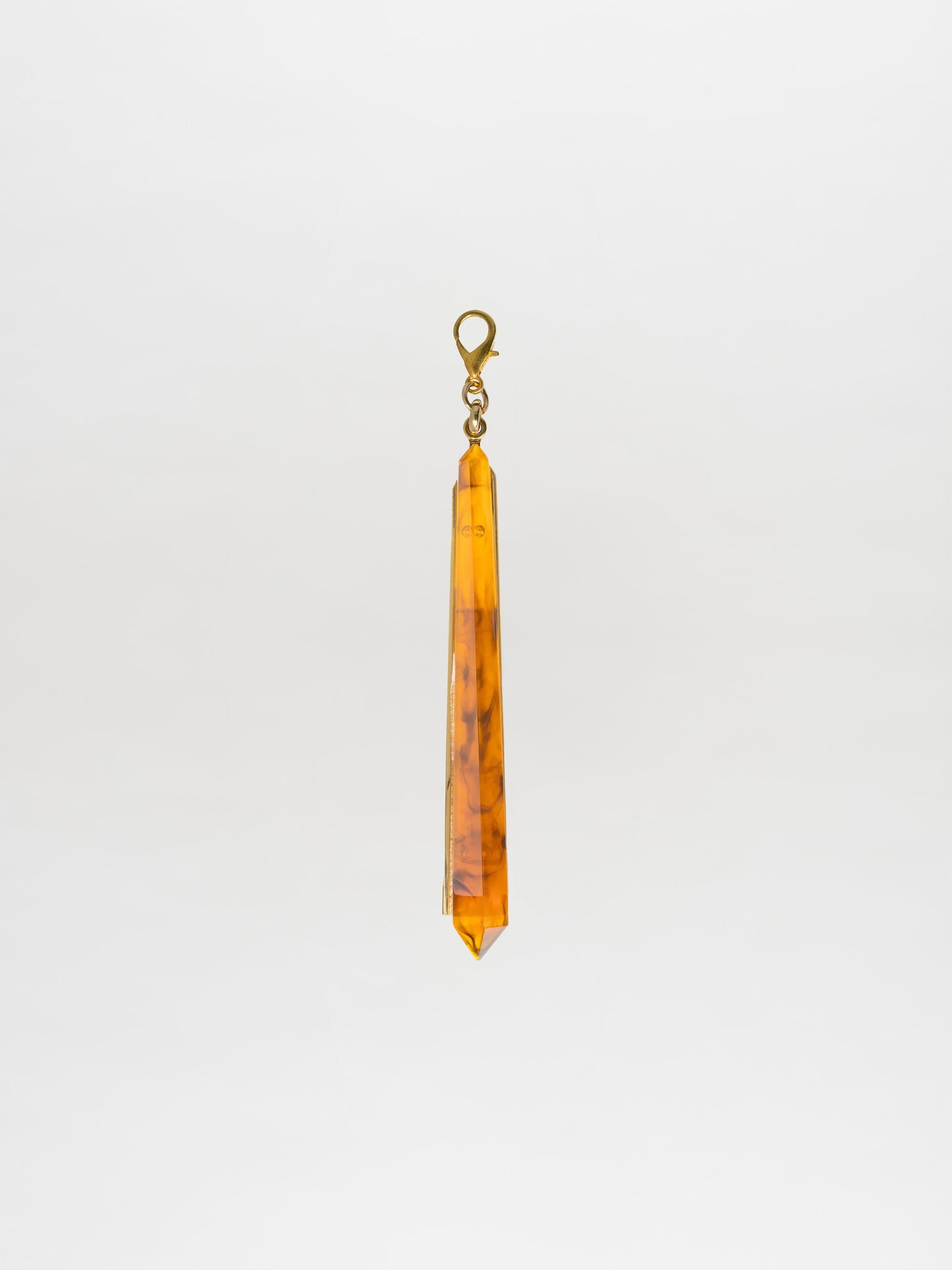 The Montse Charm Amber, an elongated crystal pendant with an amber hue and a metal clasp, is elegantly showcased against a plain white background, highlighting the sophisticated Tcherassi design.