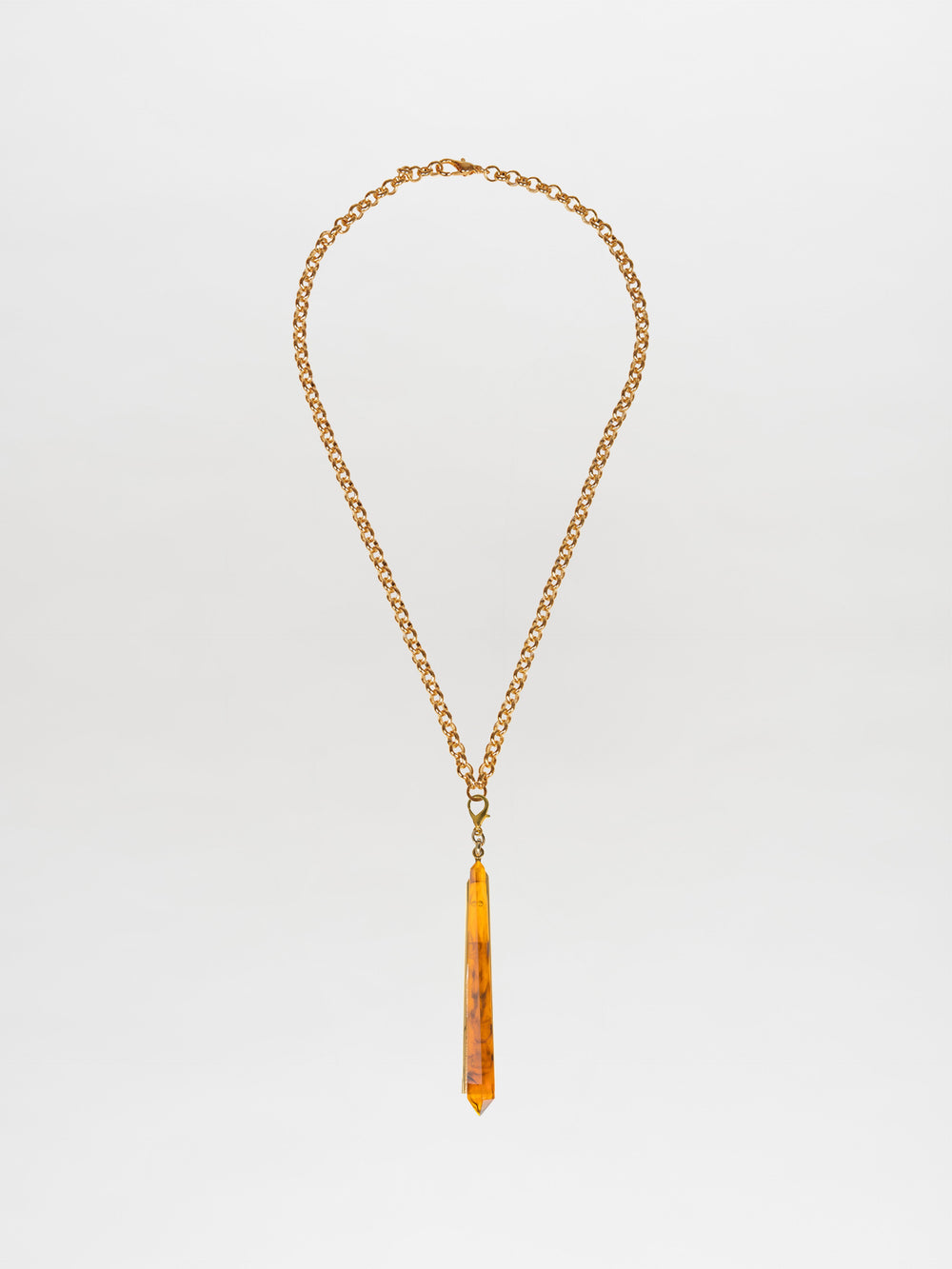 The Montse Necklace showcases a gold-plated brass chain with a long geometric amber-hued crystal pendant, elegantly centered against a plain white background.