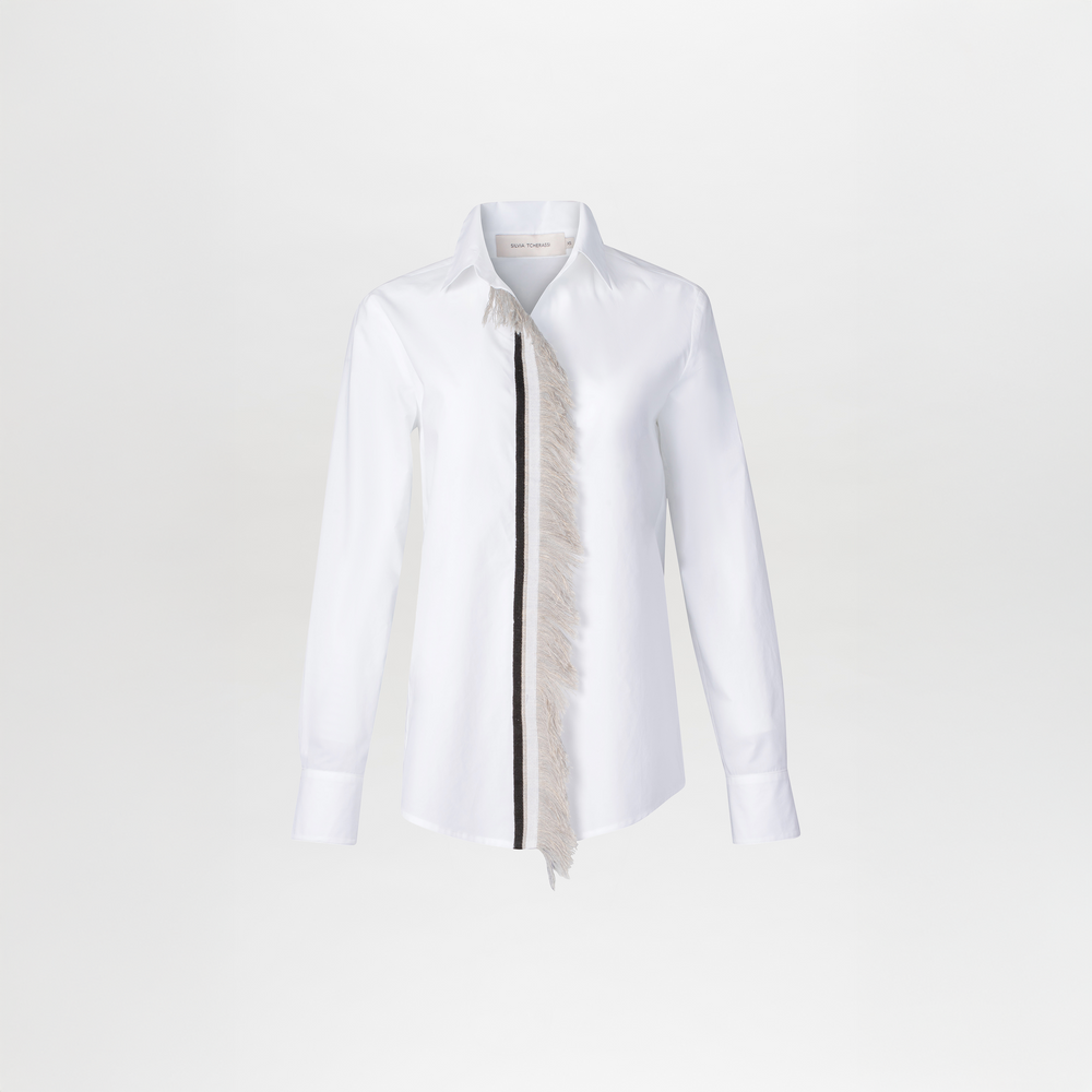 The Naroa Blouse is a white long-sleeve button-up shirt featuring a traditional collar and an asymmetrical lace fringe detail on the front.