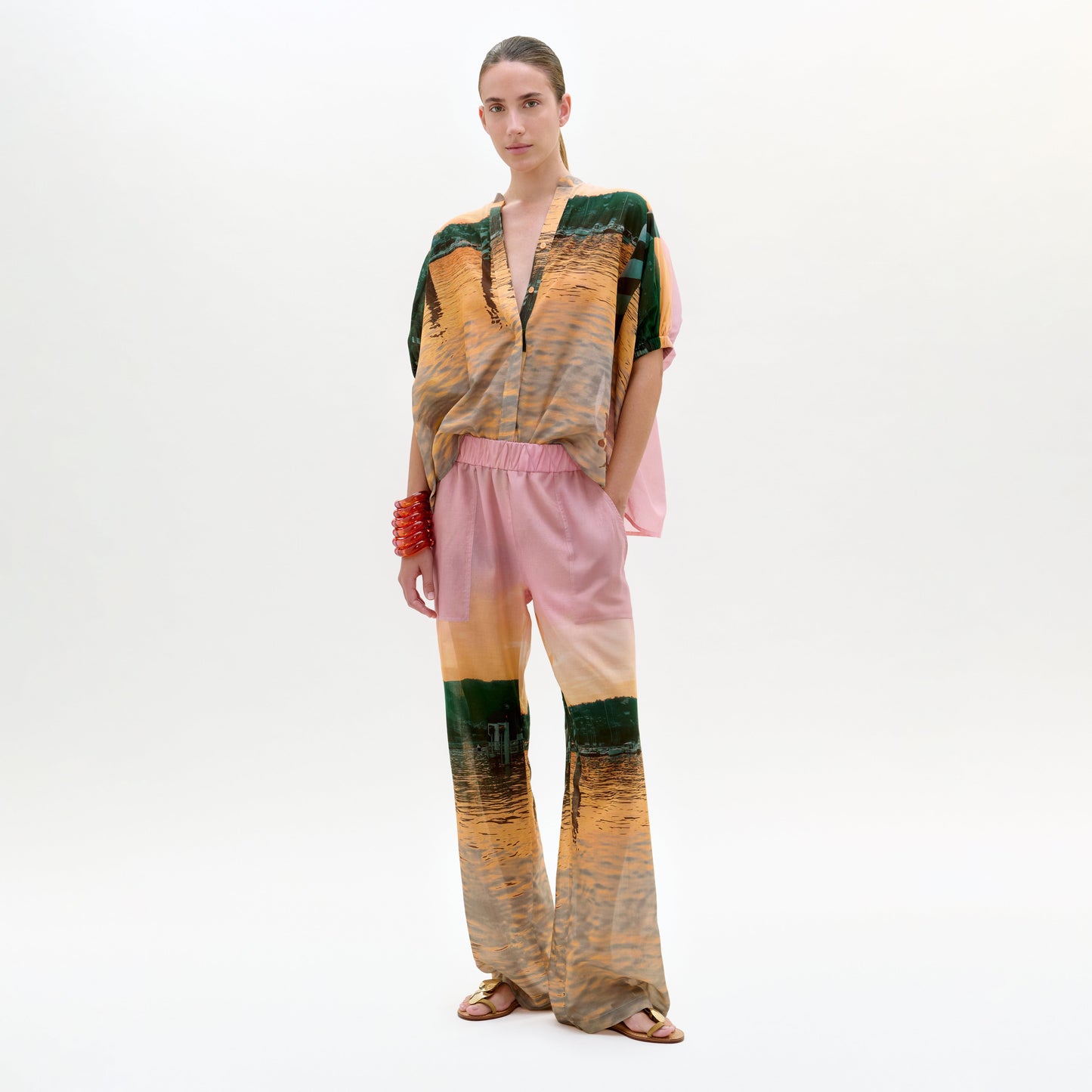 Model wearing a colorful outfit with a patterned top and pink pants on a white background
