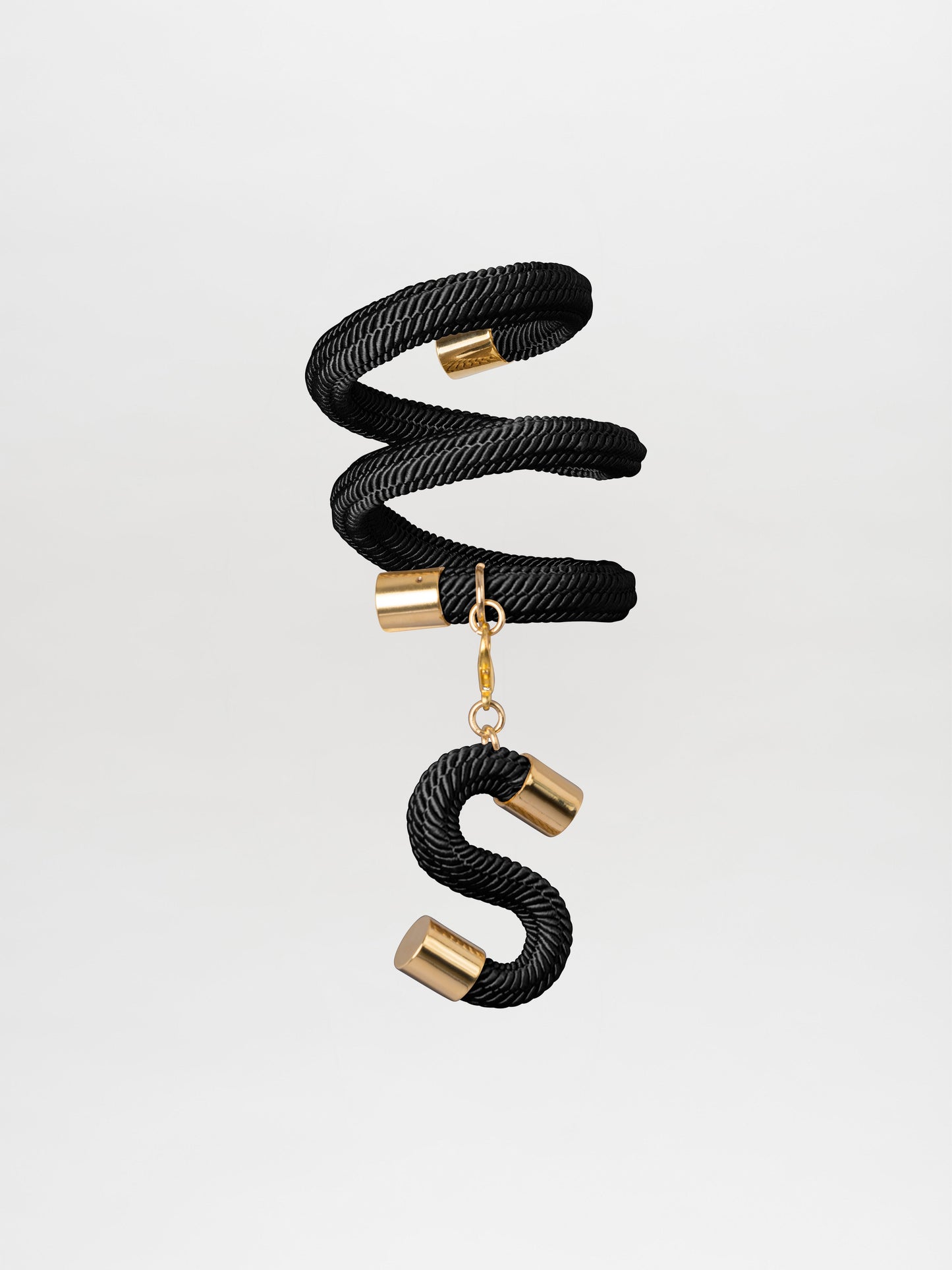 The Nicky Bracelet Black by Tcherassi showcases a unique design, featuring a black rope coiled into a spiral with gold-plated brass accents, elegantly finishing in an "S"-shaped charm.