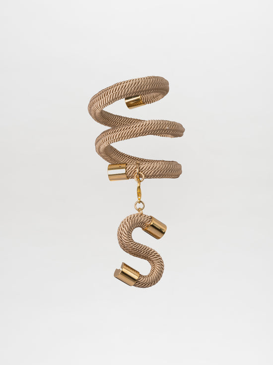 Nicky Bracelet Cream: A gold-colored, twisted rope bracelet adorned with metallic caps and a charming hanging 'S' letter, perfect for reminiscing about the elegance of bygone days on a ship.